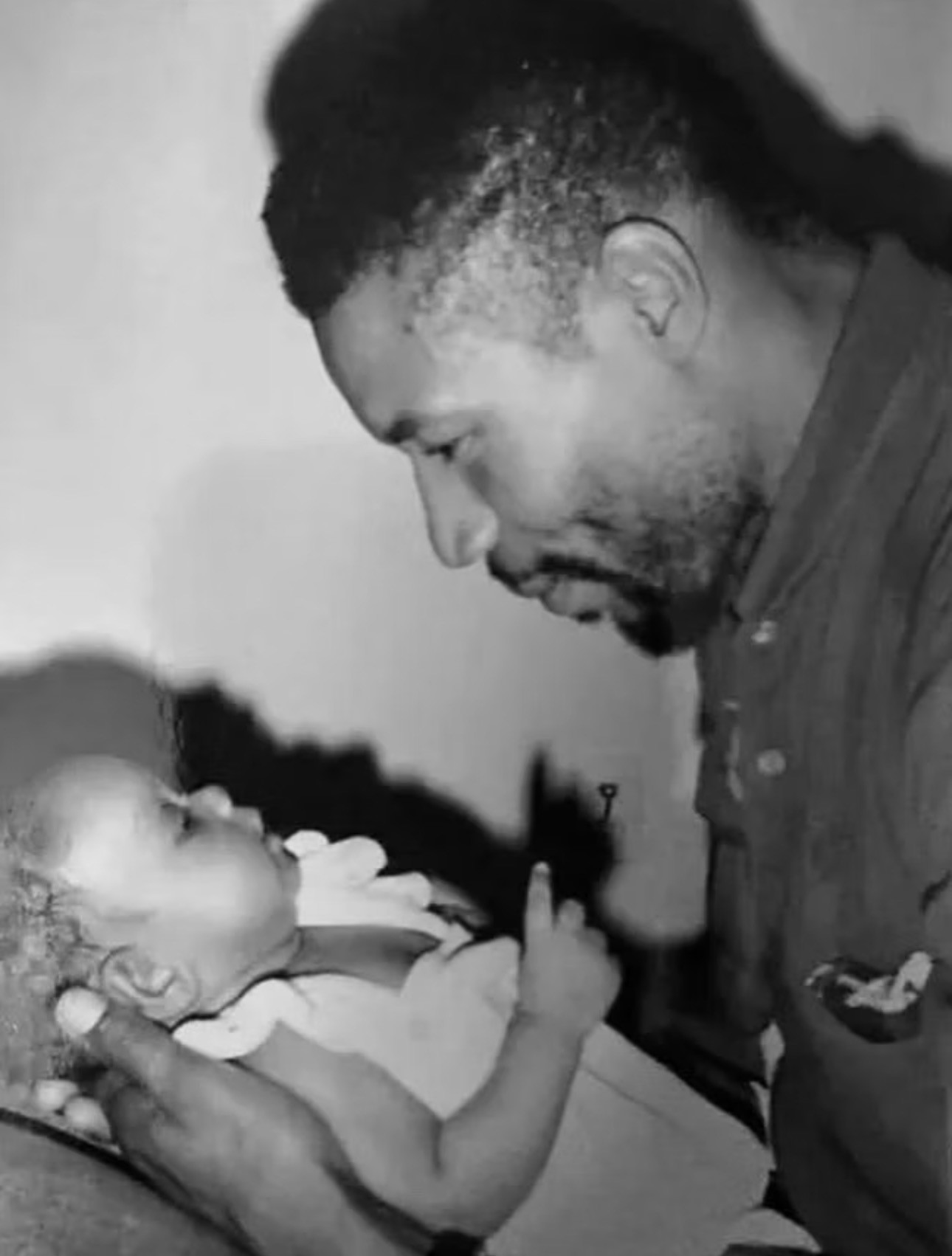 Adult man holding a baby, looking at the baby with a gentle expression, in black and white.