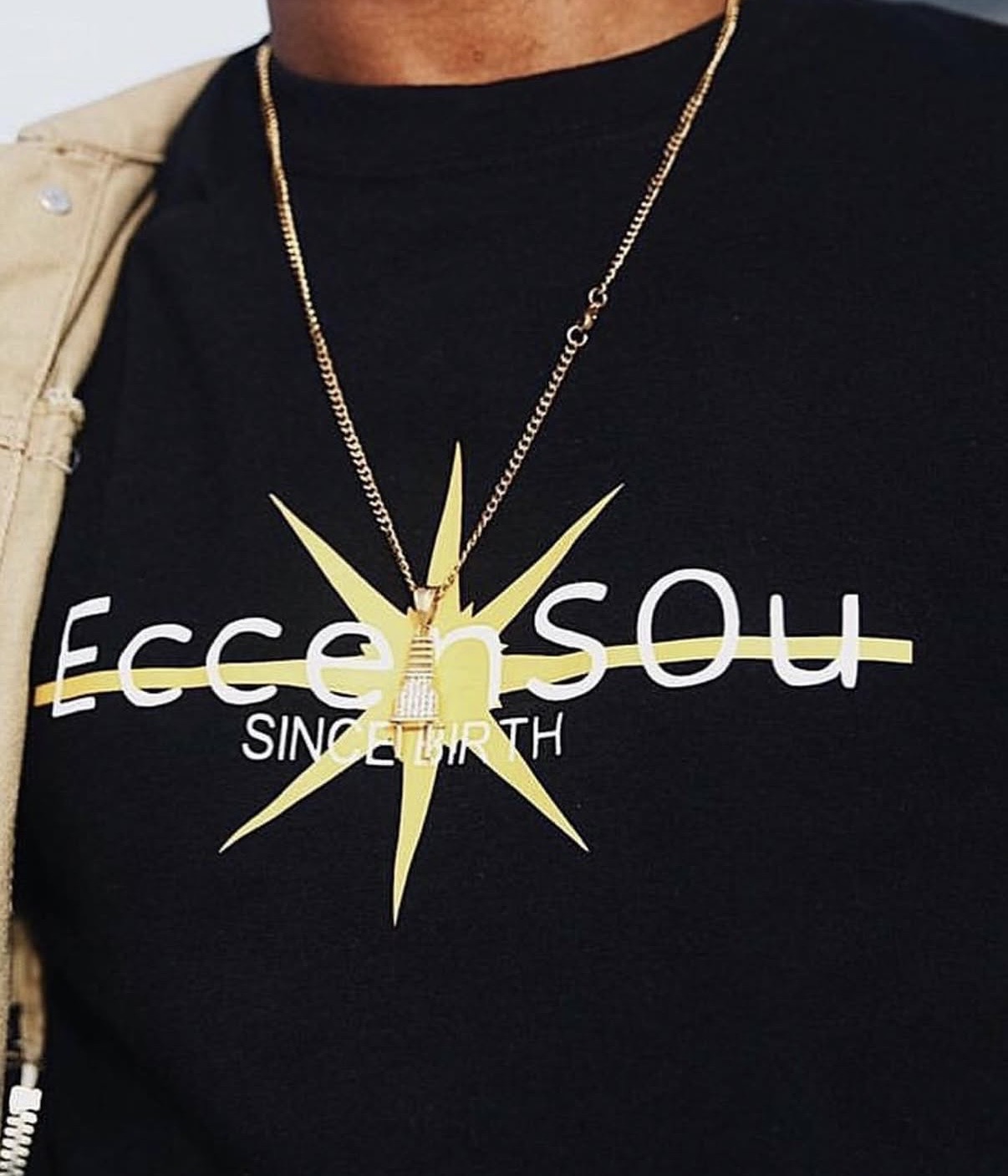 Close-up of a person wearing a black shirt with white text and a gold star-shaped necklace.