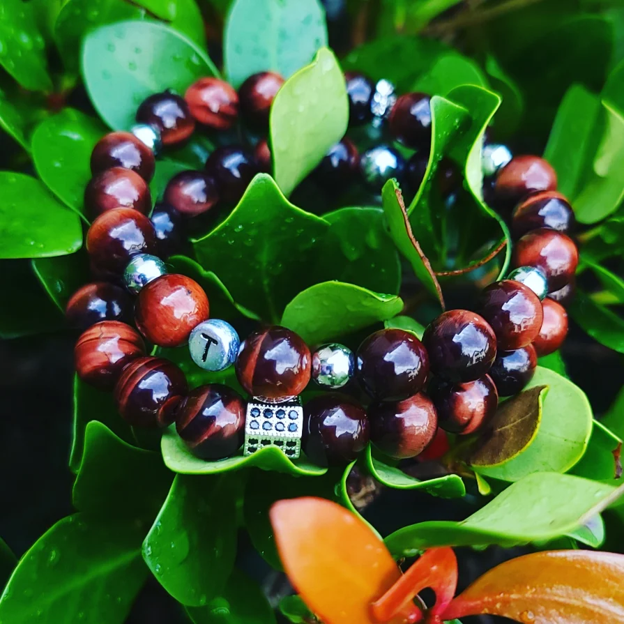 Beaded bracelet with brown, silver, and light blue beads resting on green leaves and plants.