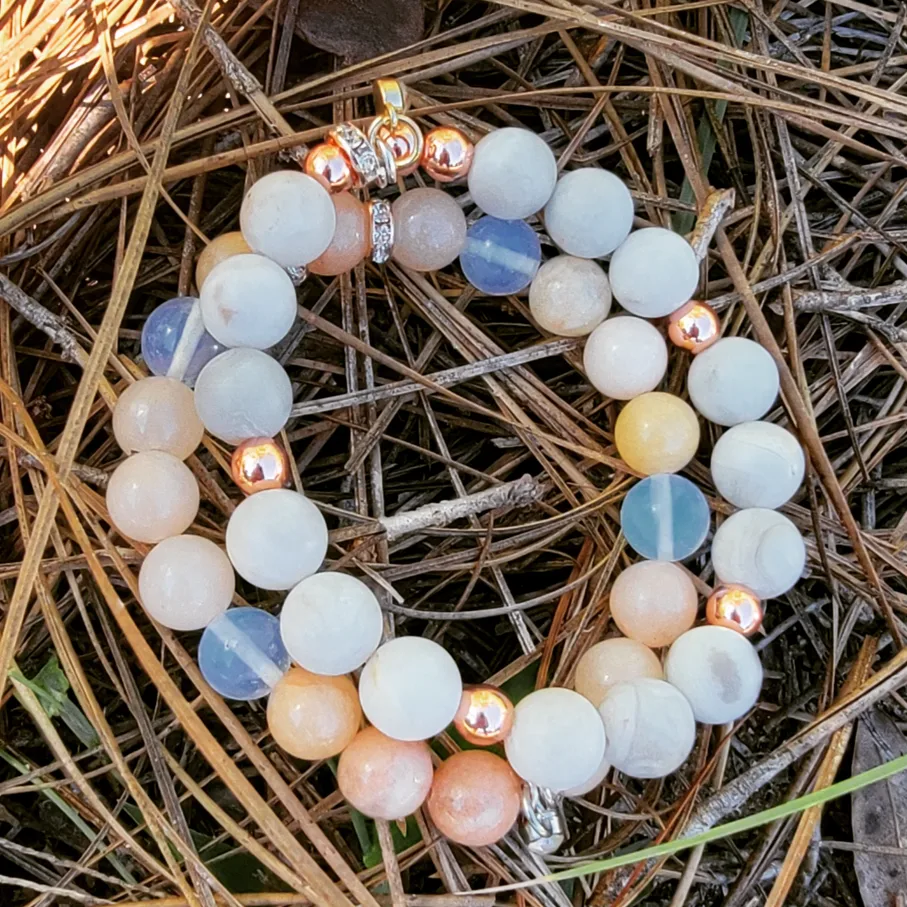 Beaded bracelet with white, blue, and metallic beads on dry grass, circular shape, close-up.