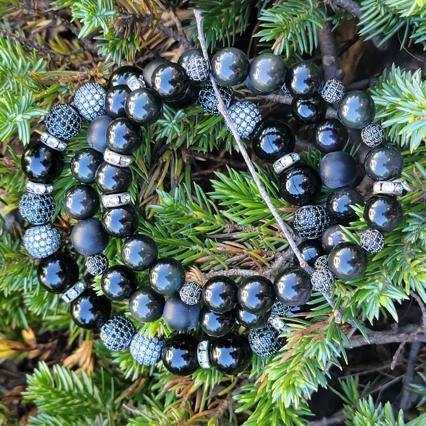 Black beaded necklace with silver accents resting on green pine branches.