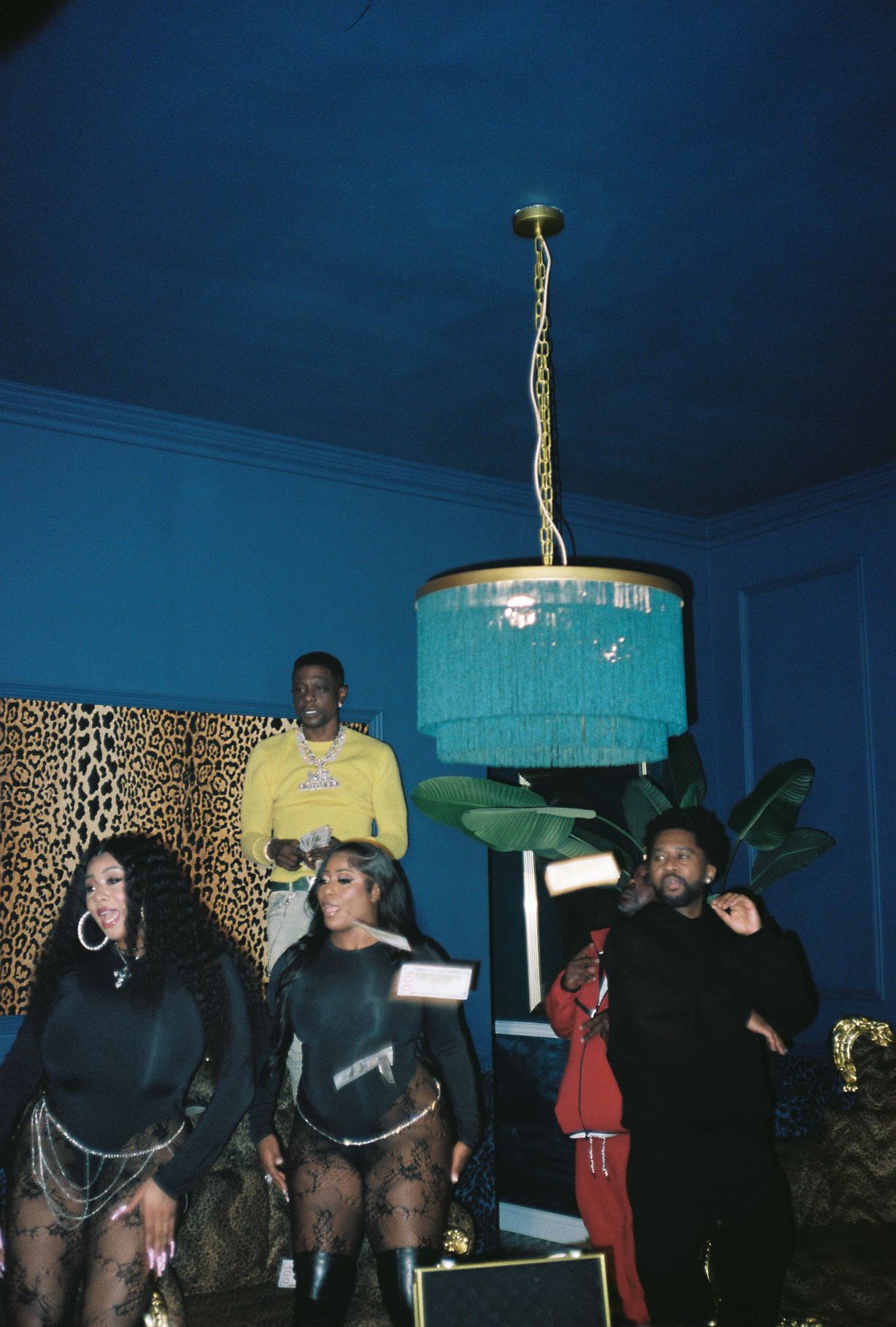 People gathered around a blue cake on a table, with a blue wall and leopard print curtain in the background.