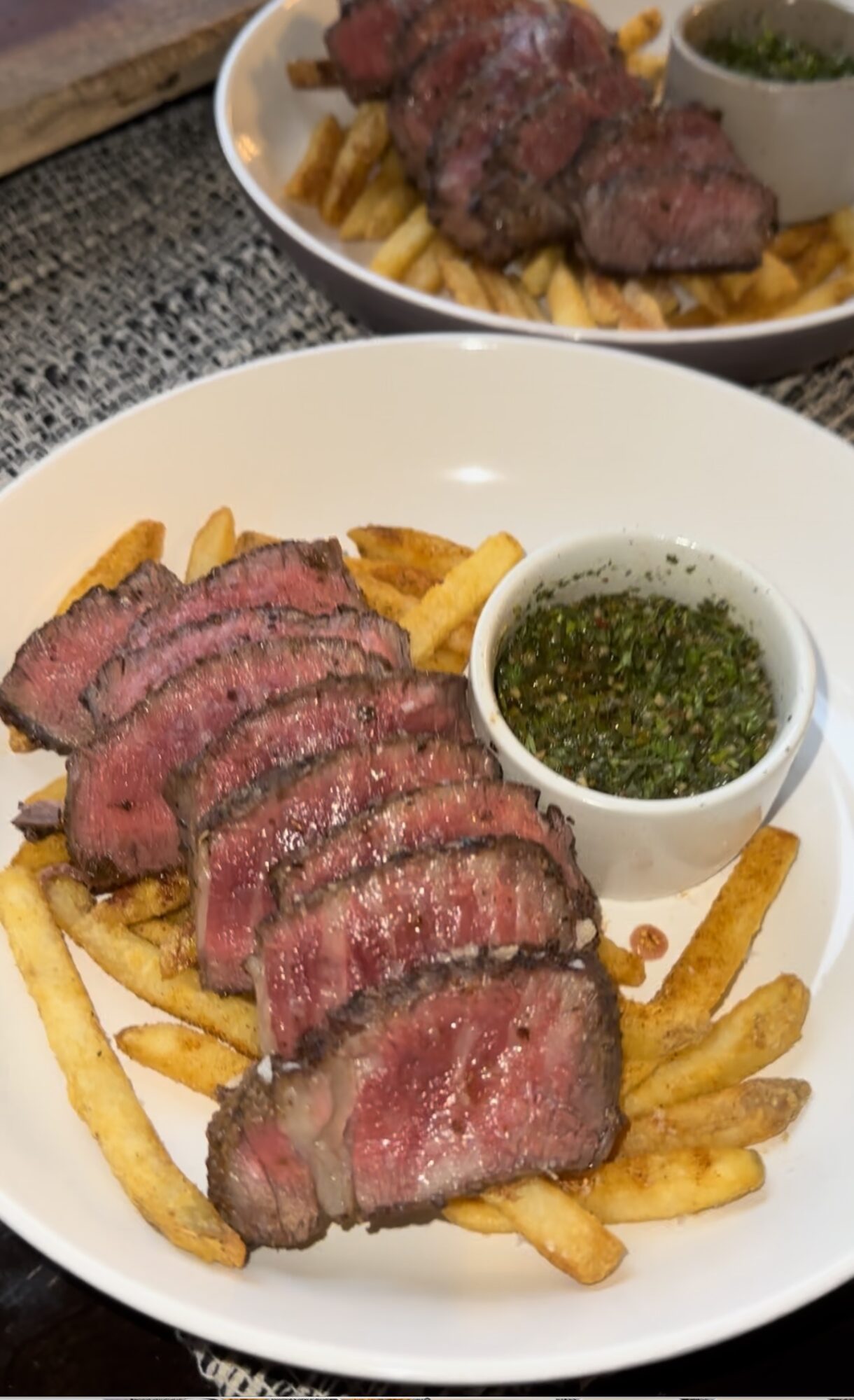Sliced cooked steak on fries with a small cup of green sauce in a white bowl.