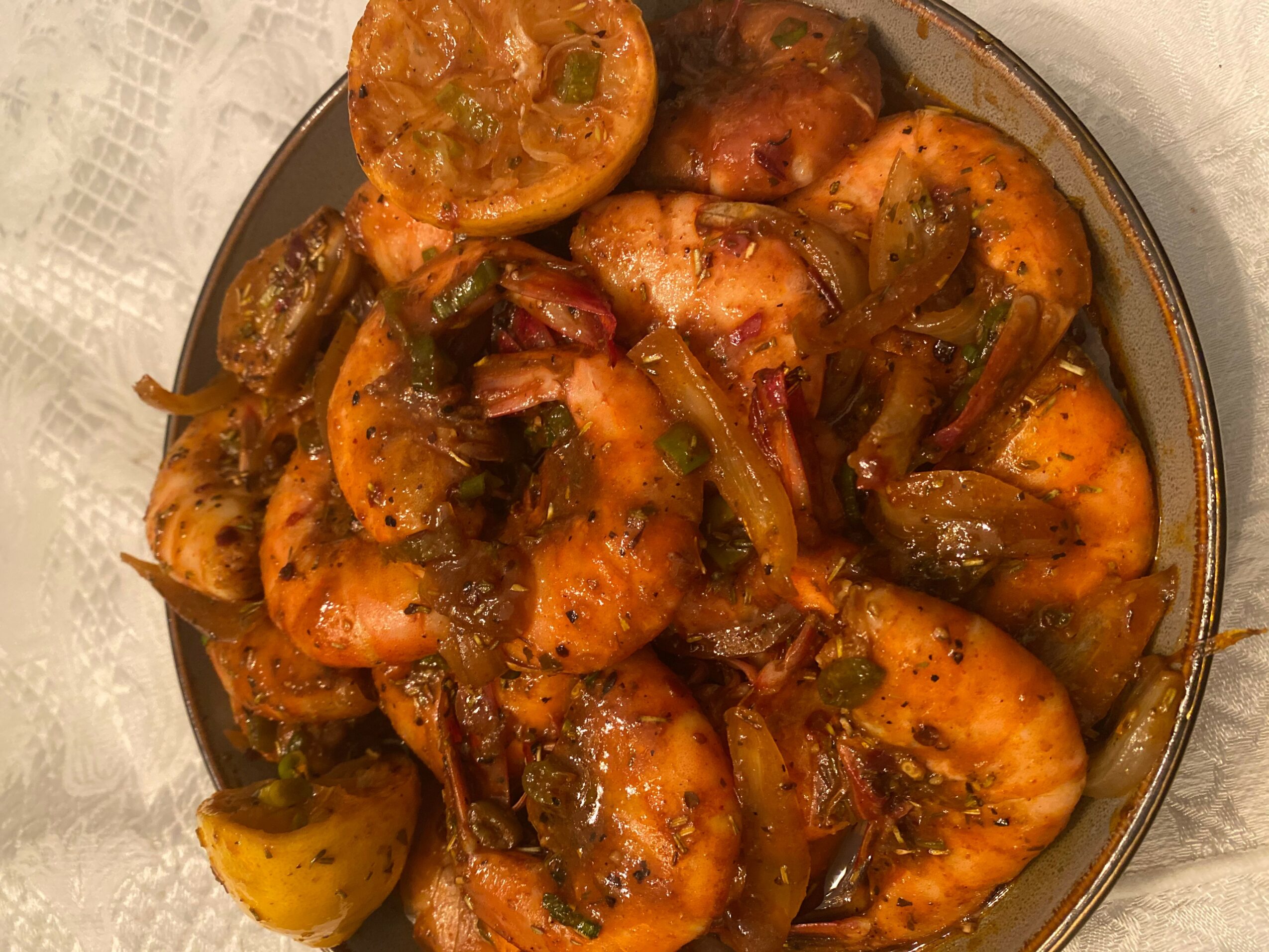 Plate of cooked shrimp with vegetables and sauce, garnished with lemon slices, on a table surface.