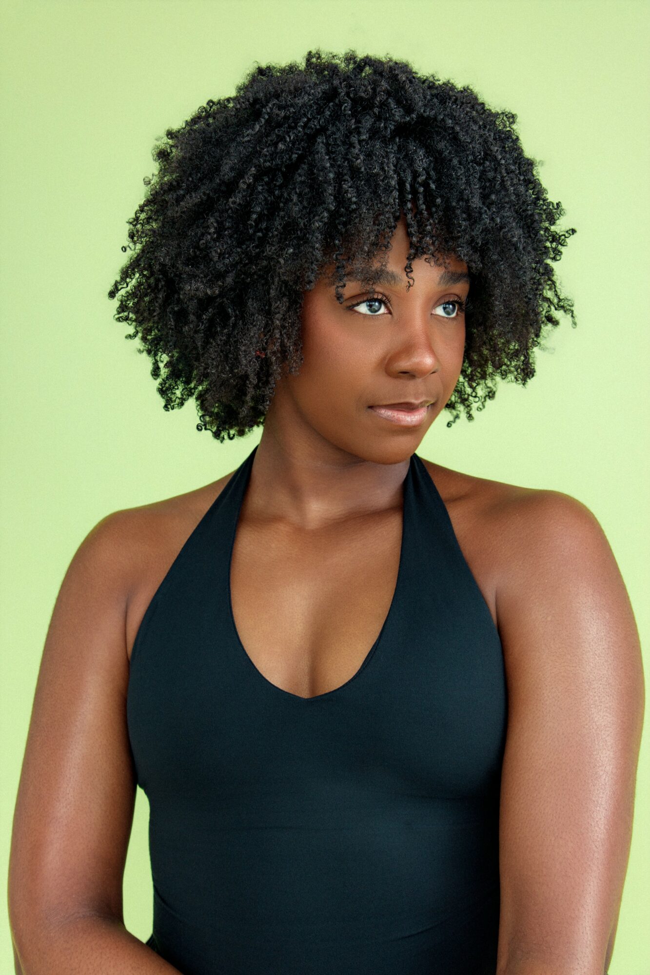 Woman with curly hair wearing a black top against a light green background.