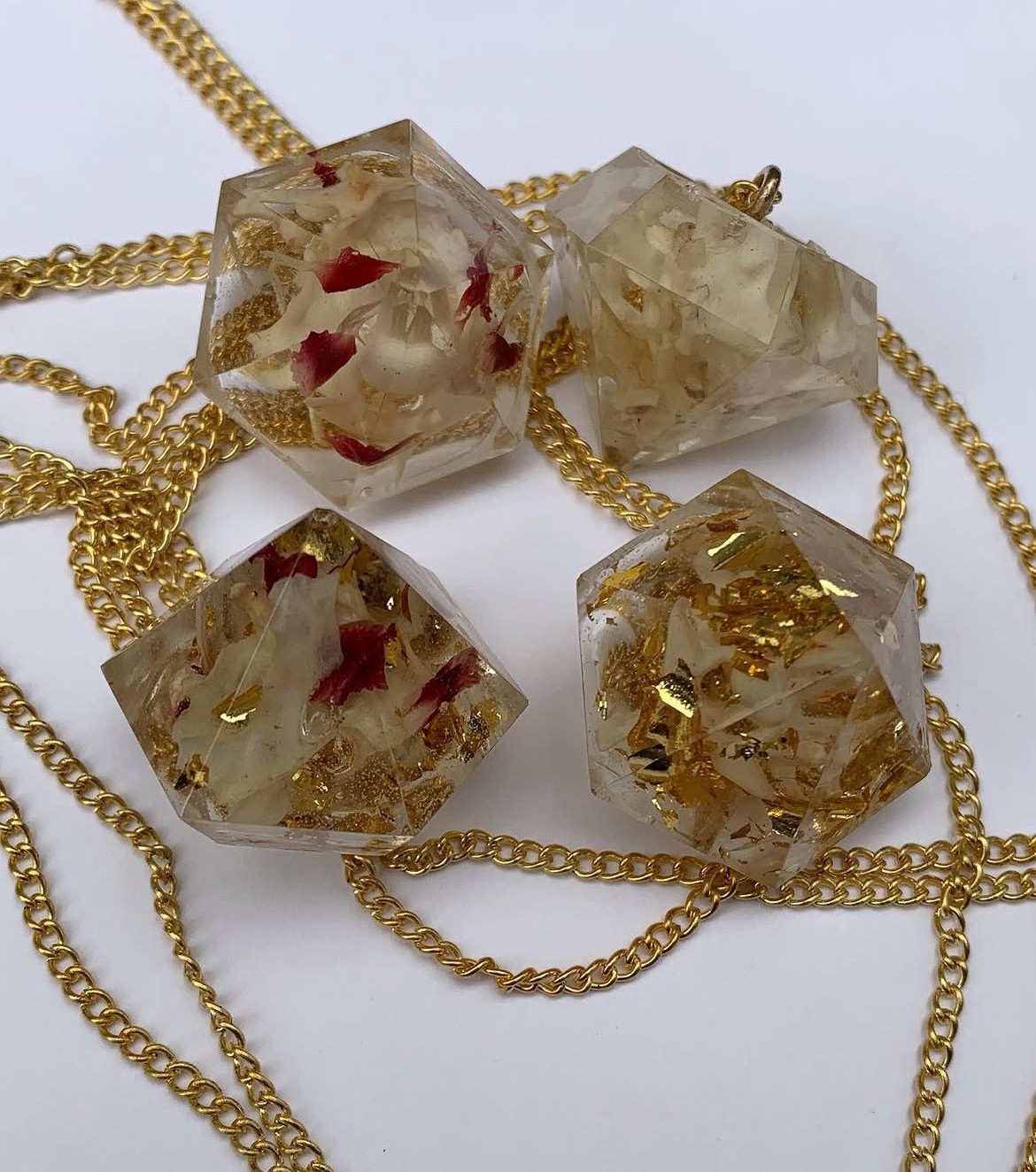 Four transparent resin cubes with red and gold inclusions, connected by gold chains, on a white background.