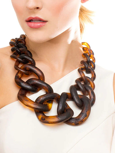 Close-up of a woman wearing a large, chunky tortoiseshell necklace, with part of her face and shoulder visible.