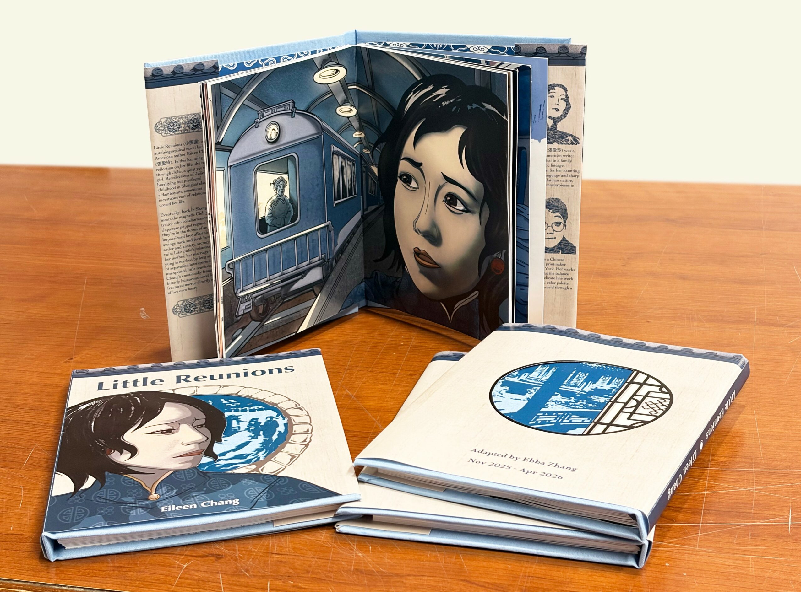 Open book with a woman's face illustration, two closed books with similar artwork, on a wooden surface.