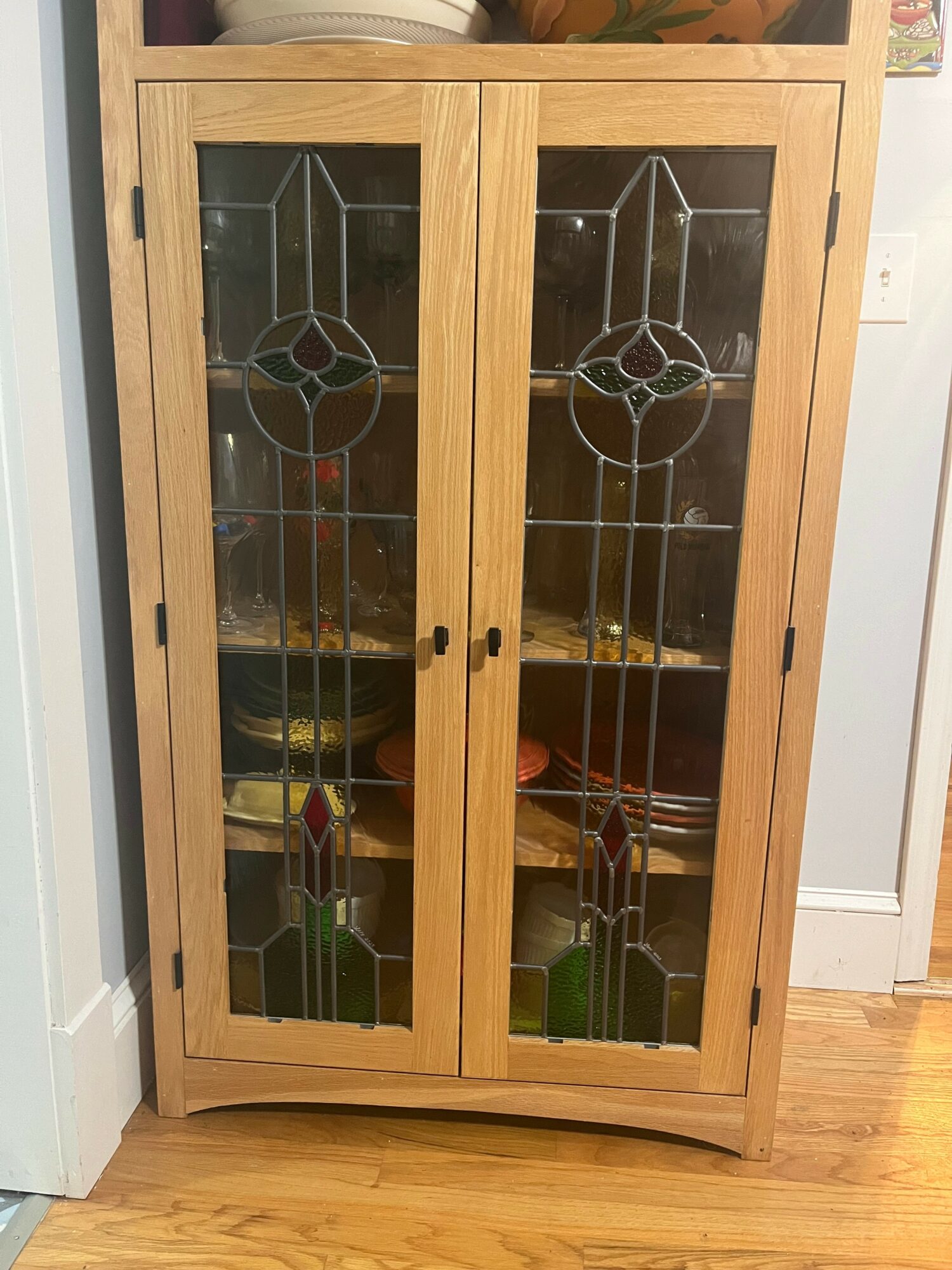 Wooden cabinet with glass doors and decorative stained glass panels, standing on a hardwood floor.