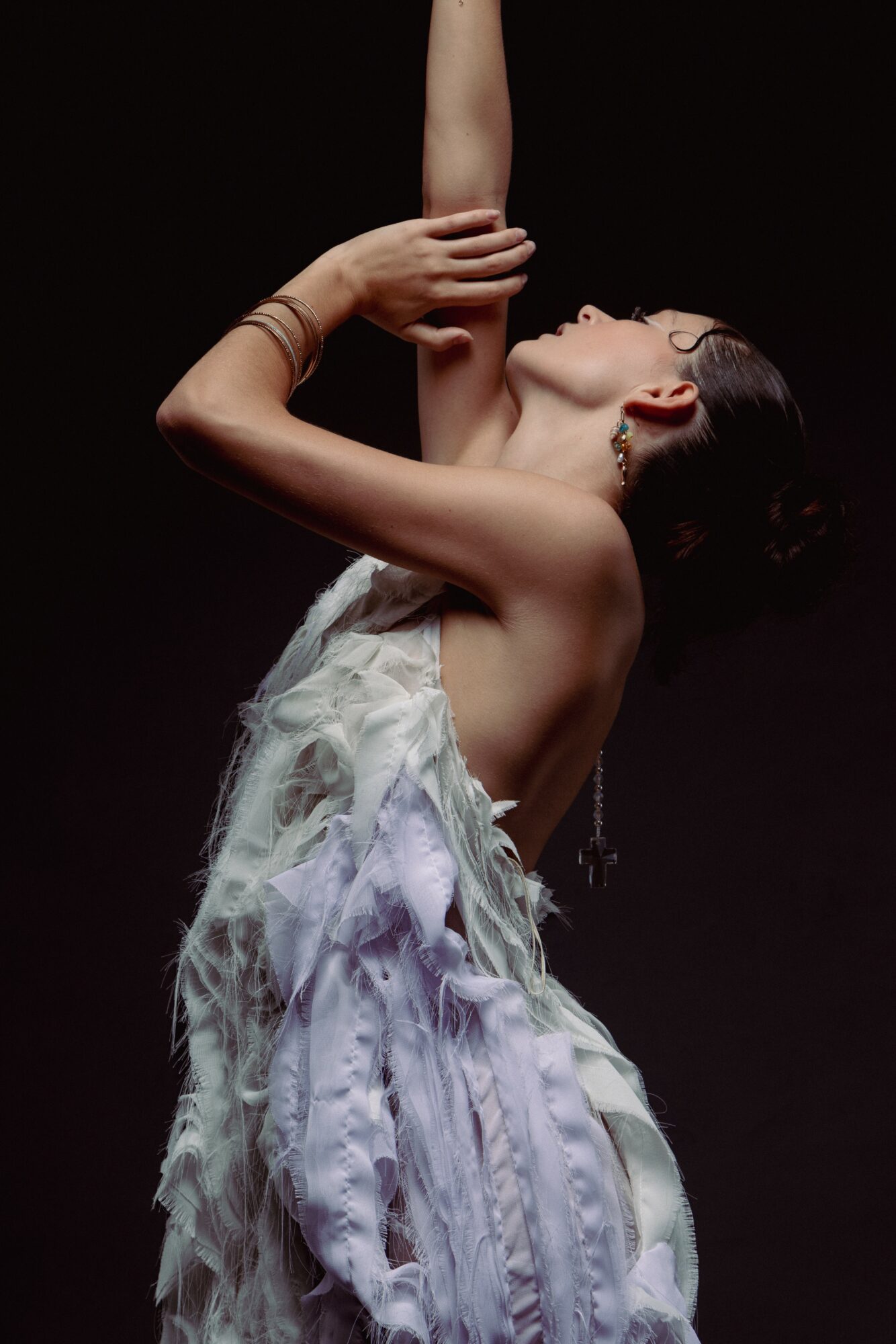 Woman in a flowing dress with arms raised, head tilted back, dark background, artistic pose.