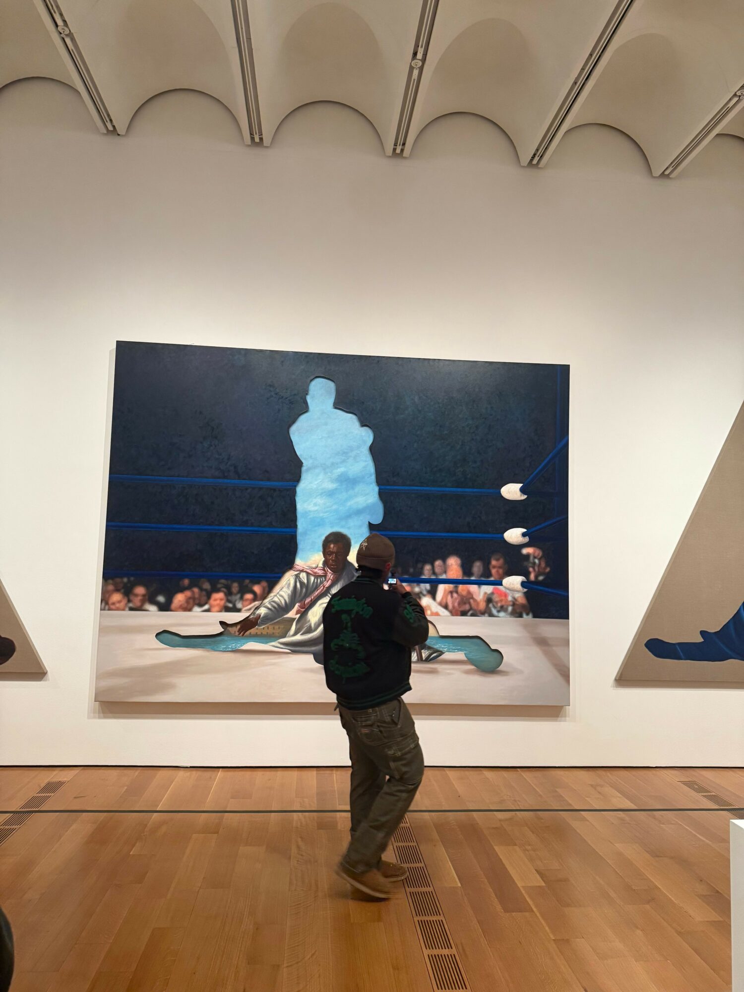 Person standing in front of a large painting in an art gallery, wooden floor, white wall, abstract cityscape scene.