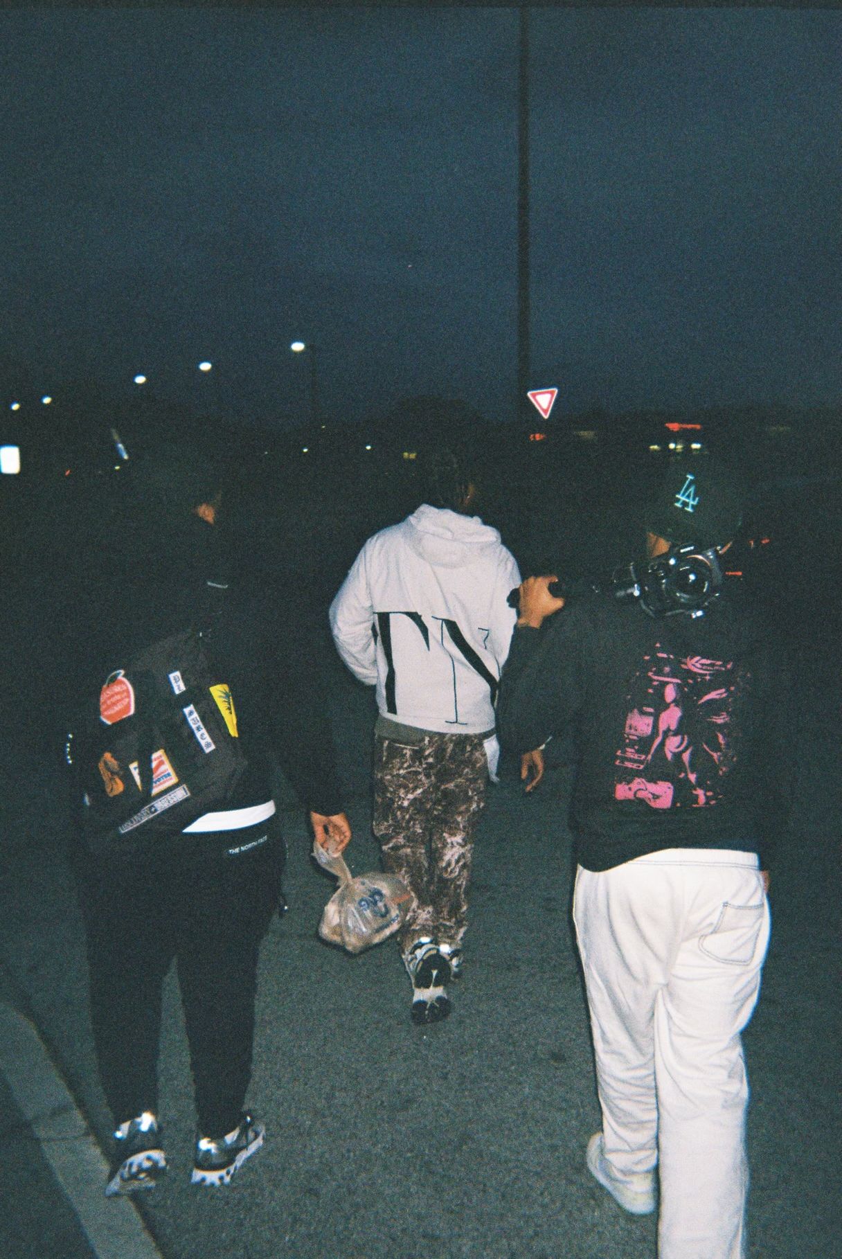 Group of people standing outdoors at night, some wearing jackets and masks, with a dark background.