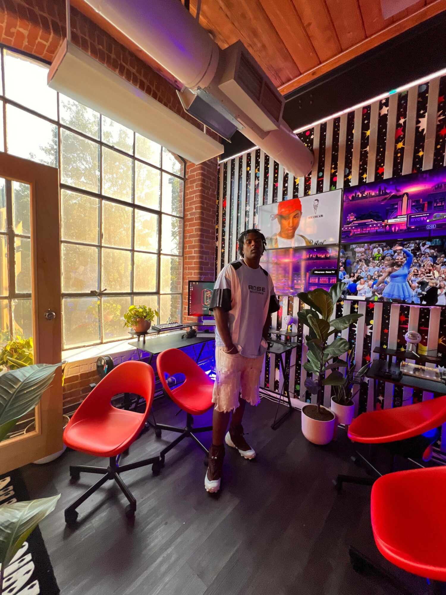 Person standing in a modern office with red chairs, large window, and colorful wall art.