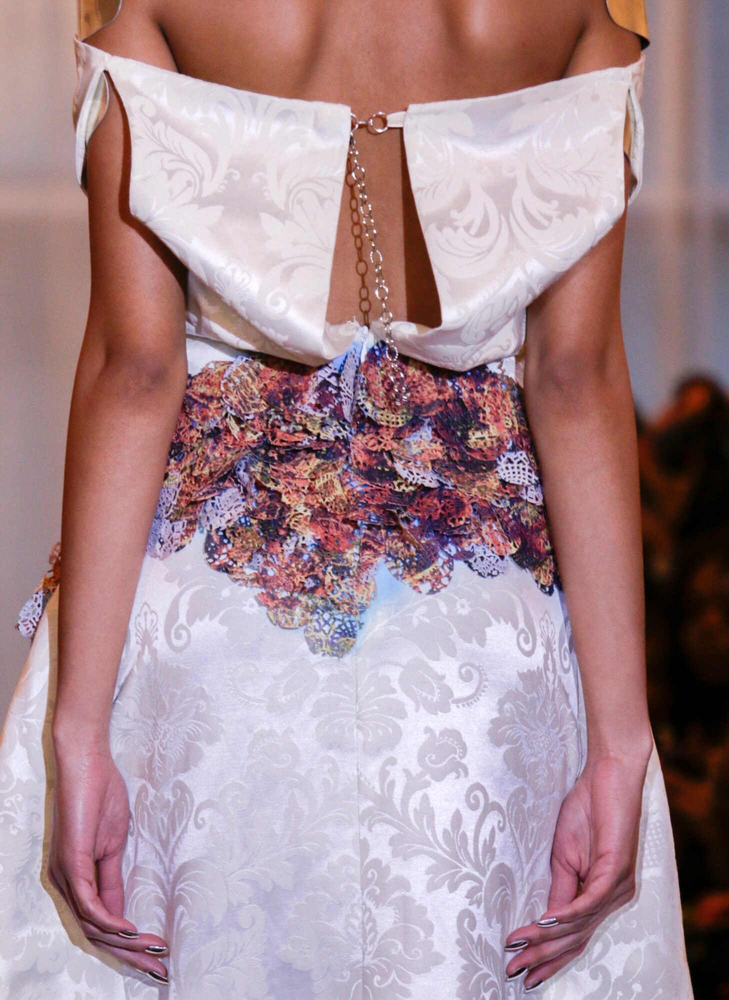 Close-up of a model wearing a white off-shoulder top with a chain detail and a floral skirt with purple, pink, and orange flowers.