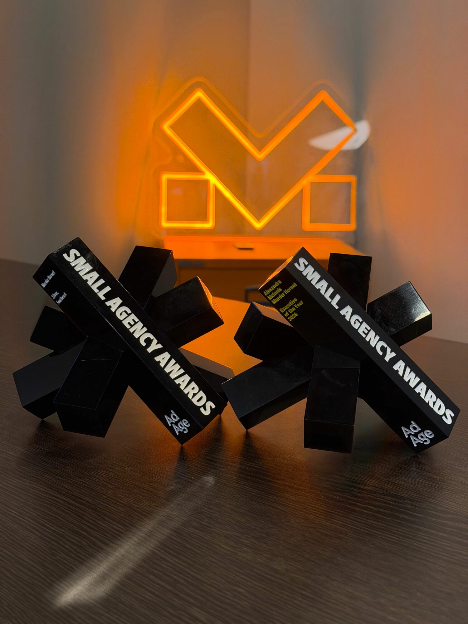 Black awards with white text stacked on a dark surface, with a glowing orange logo in the background.