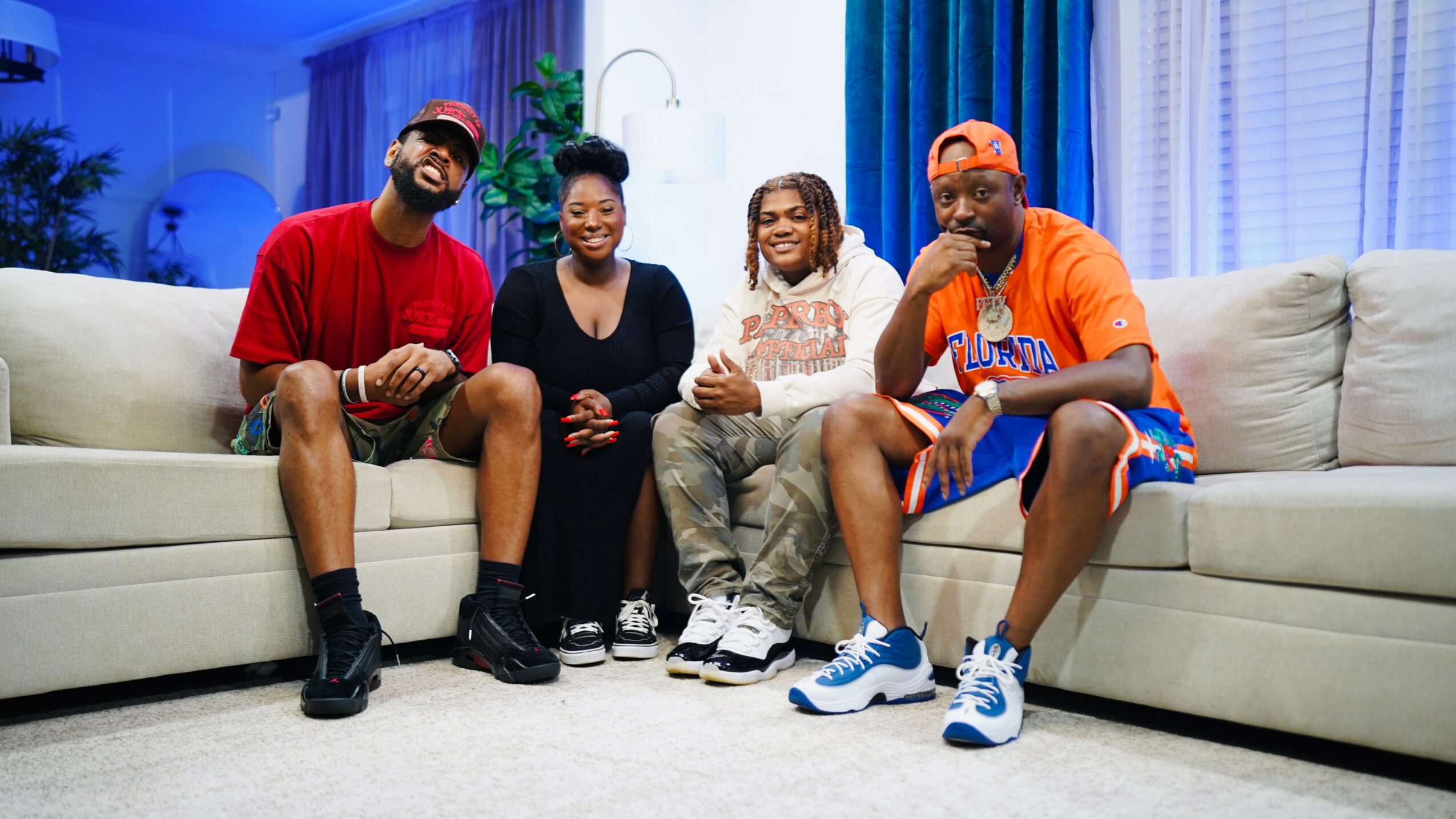 Four people sitting on a light-colored sofa in a living room, smiling and enjoying each other's company.