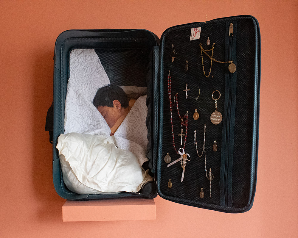 Open jewelry case with necklaces and earrings, and a baby sleeping inside a box, on a pink background.