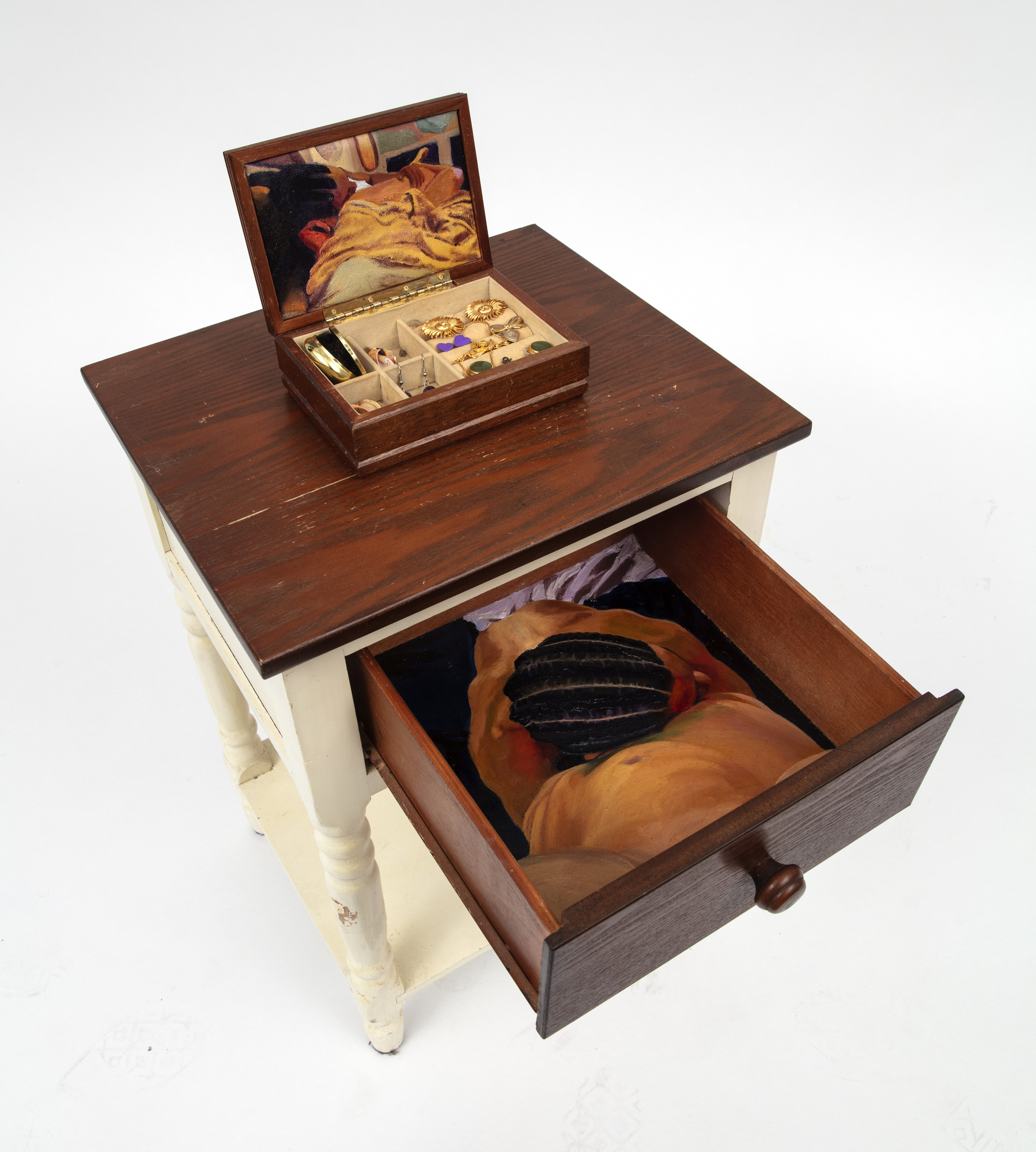 A small table with a drawer open, showing a person with braided hair inside. A jewelry box with a mirror is on top.