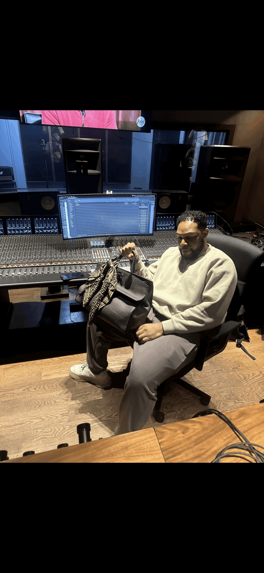 Person sitting in a recording studio with audio equipment and speakers, wearing a white hoodie and face mask.
