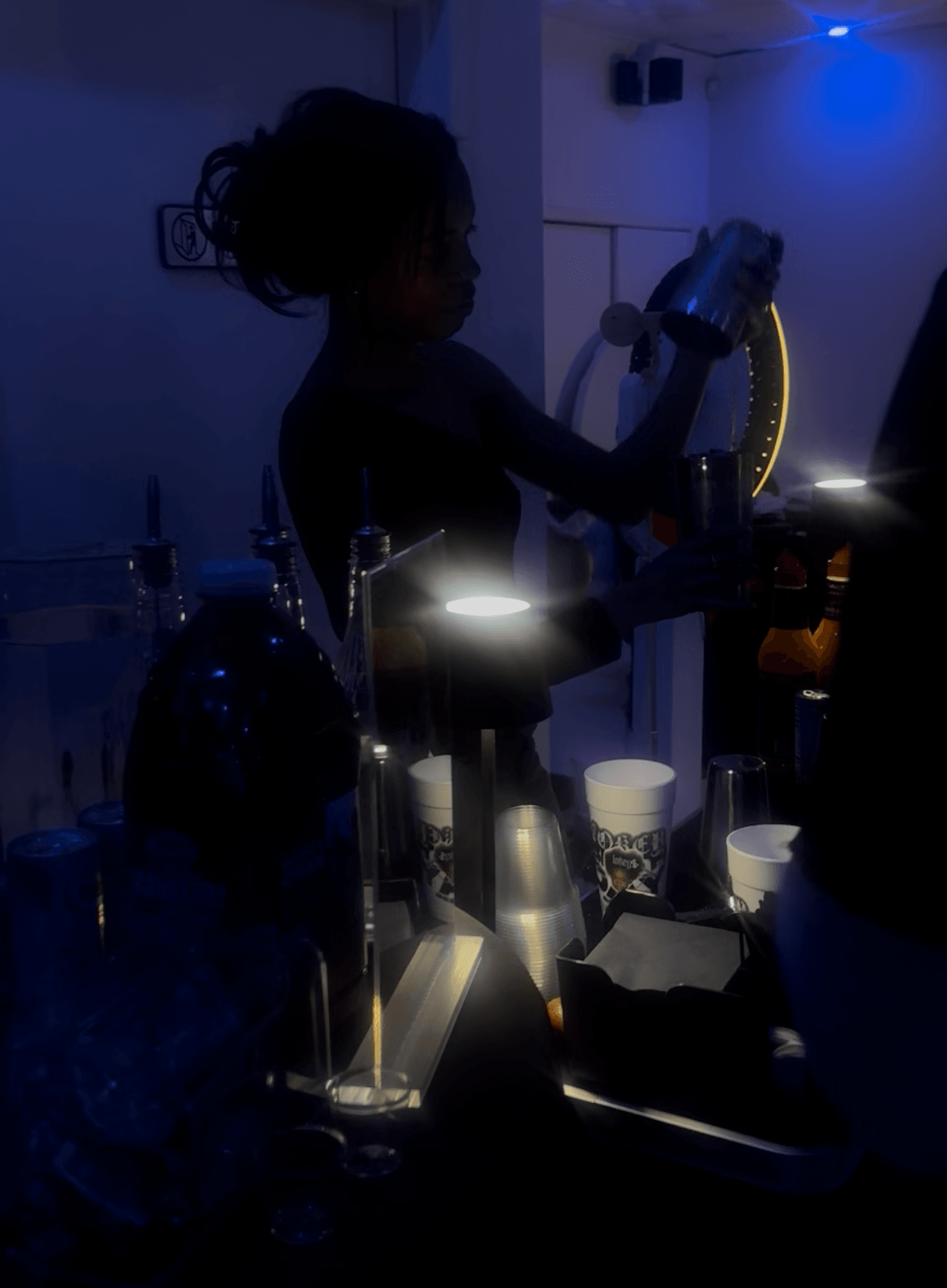 Child with curly hair using a blender in a dimly lit room, illuminated by small lights on the counter.