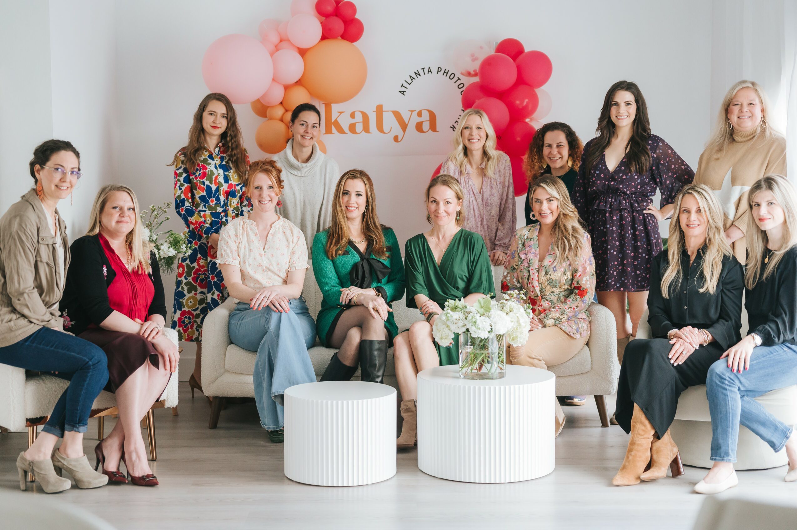 Group of women sitting and standing in a decorated room with balloons and flowers, smiling for a photo.