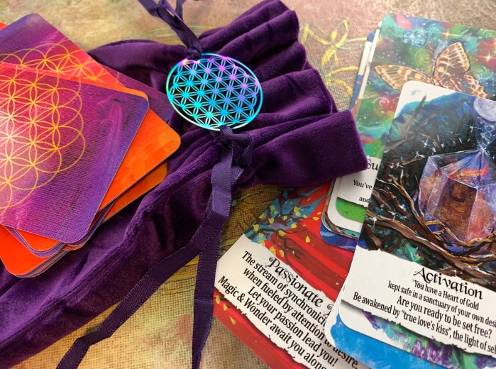 Purple velvet bag with a blue geometric pendant, tarot cards, and crystals on a surface.