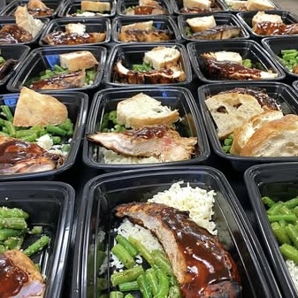 Multiple black meal containers filled with meat, vegetables, and bread, arranged in rows on a surface.