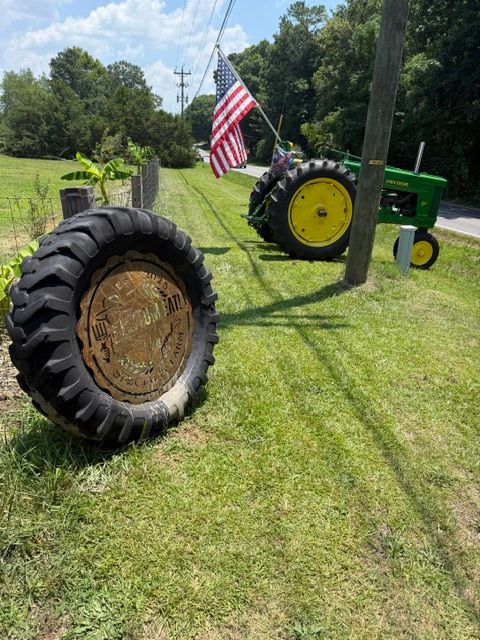 Tire with a metal emblem in the center, placed on grass, with a tractor and American flag in the background.