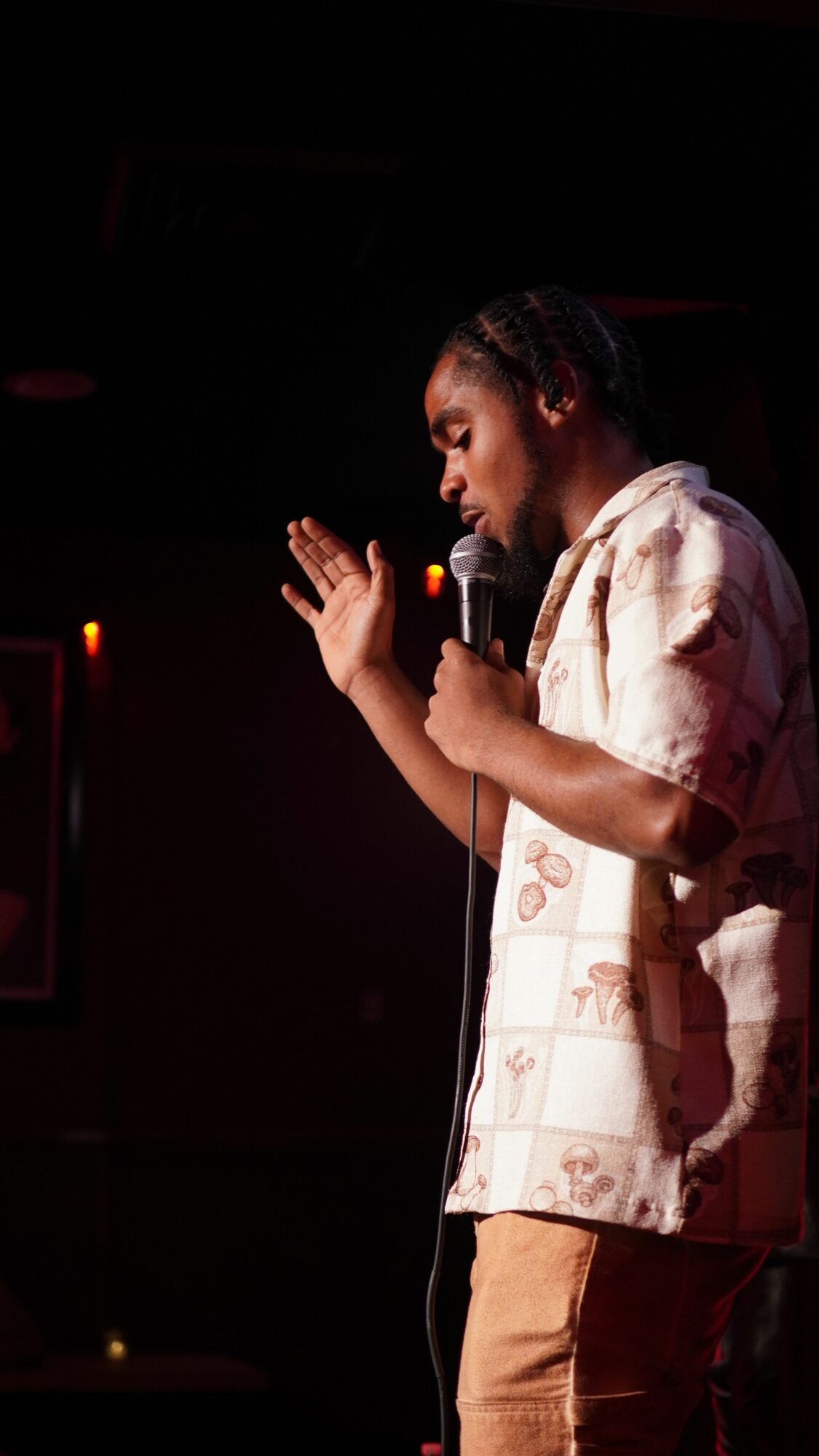Person lying on stage, holding a microphone, performing under dim lighting, with a dark background.