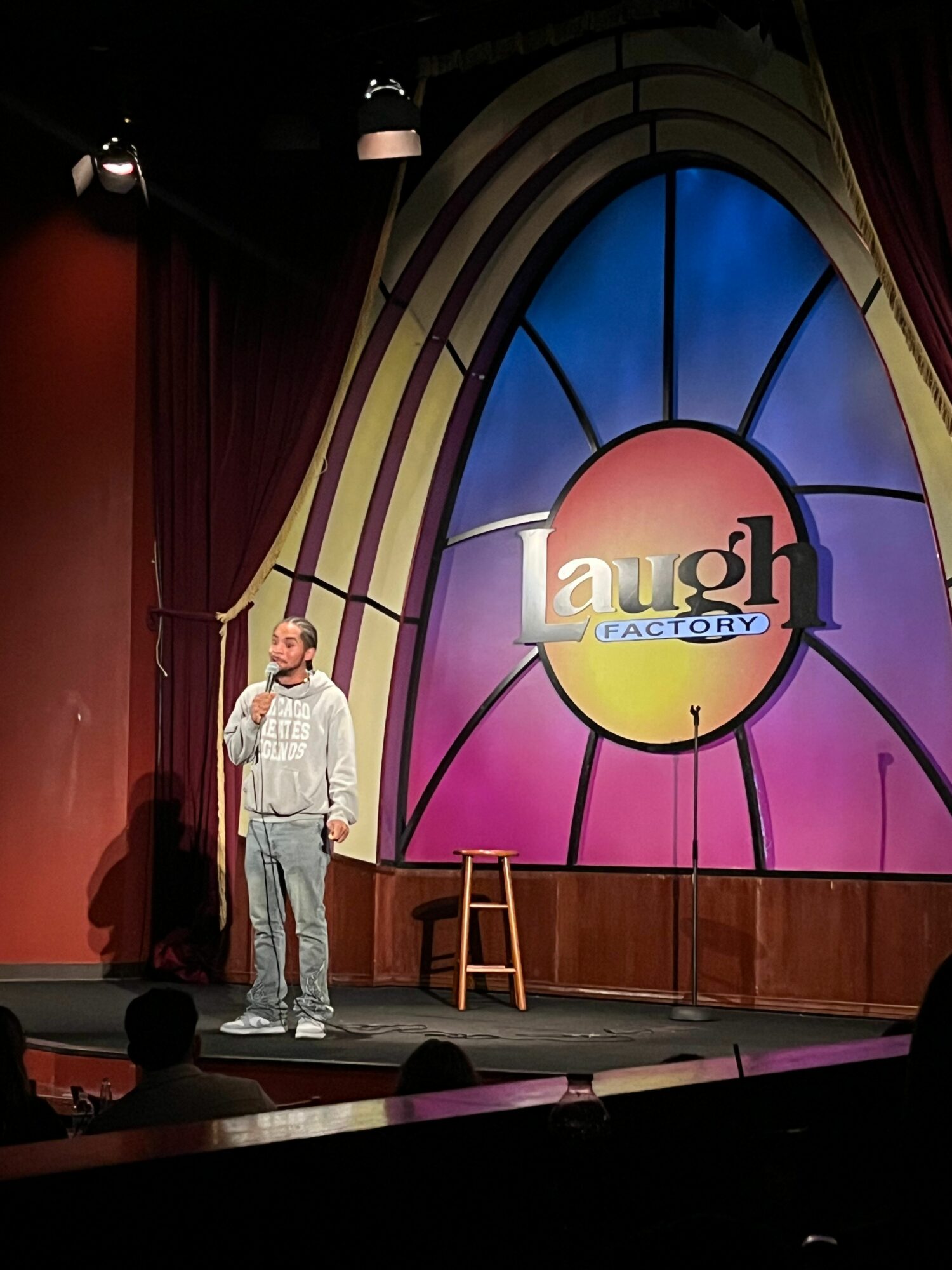 Person standing on stage with colorful stained glass window backdrop and a wooden chair.