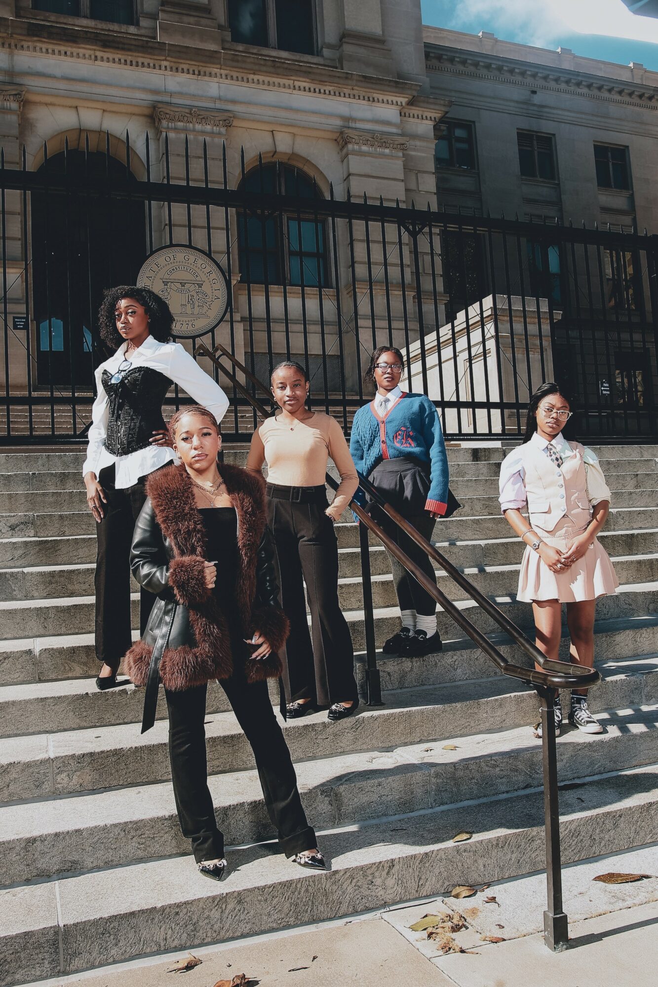 Five women stand on outdoor stairs in front of a historic building with a black fence, posing confidently.