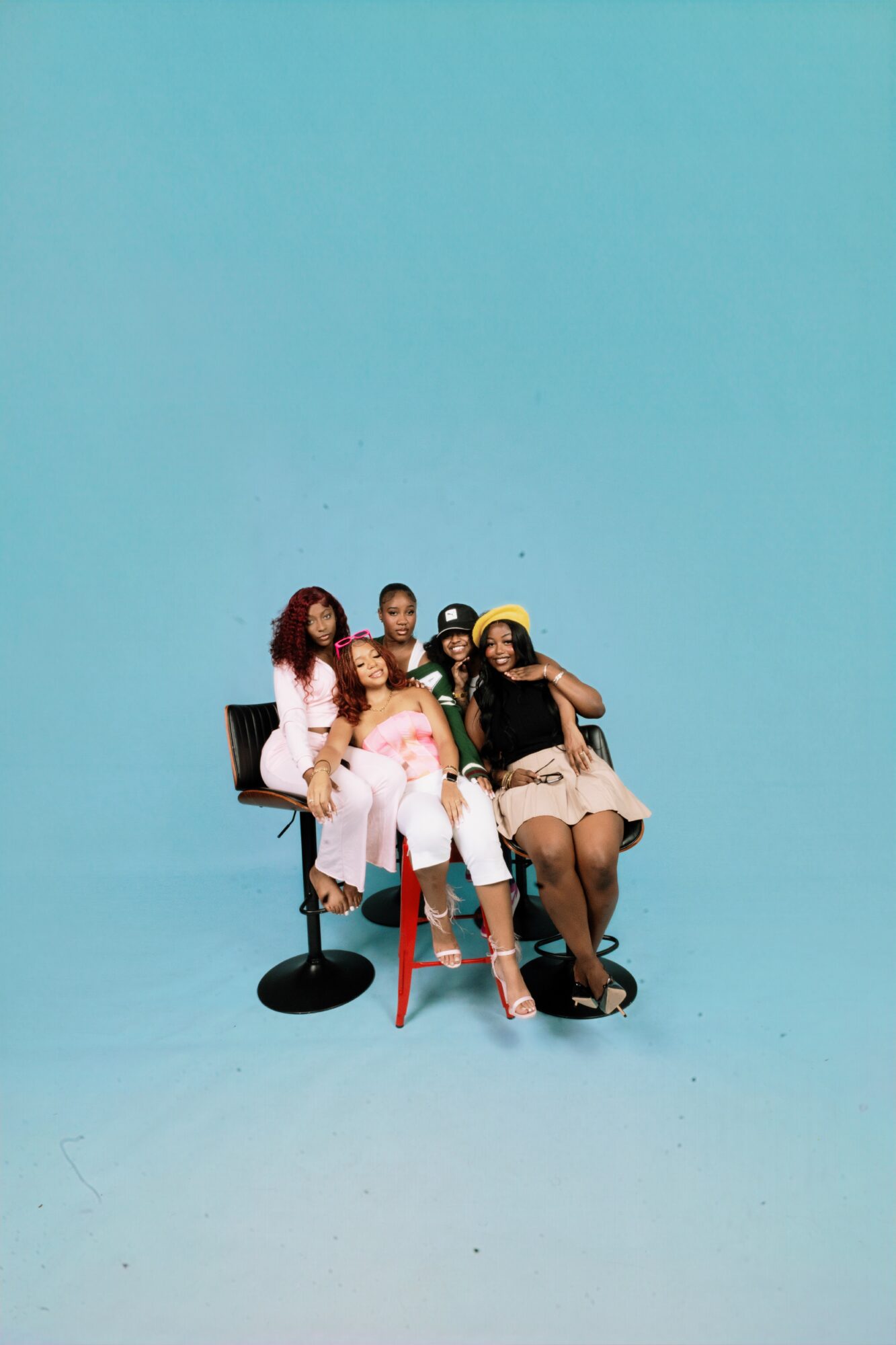 Five women sitting on chairs against a blue background, posing for a photo.