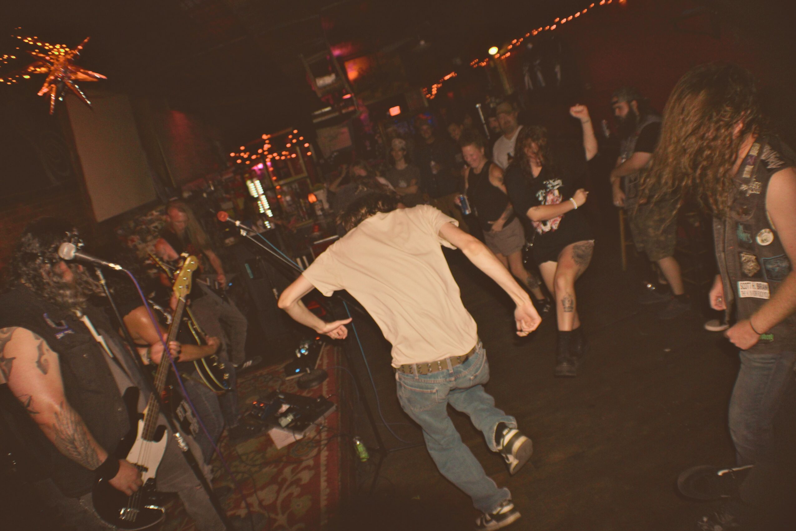 People dancing and playing instruments in a dimly lit indoor venue with colorful lights.