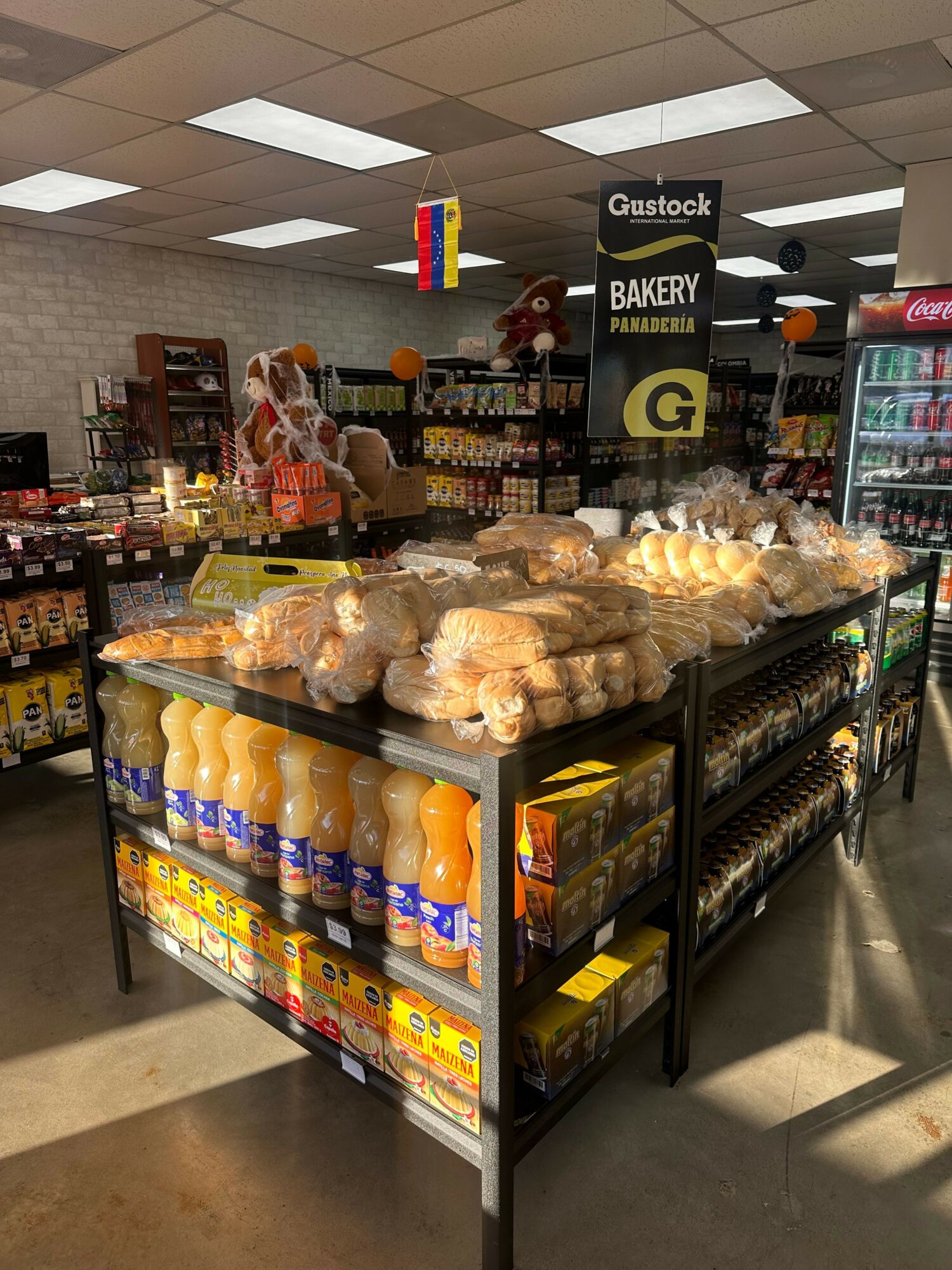 Grocery store aisle with baked goods and snacks on display, shelves stocked with various products, and overhead lighting.