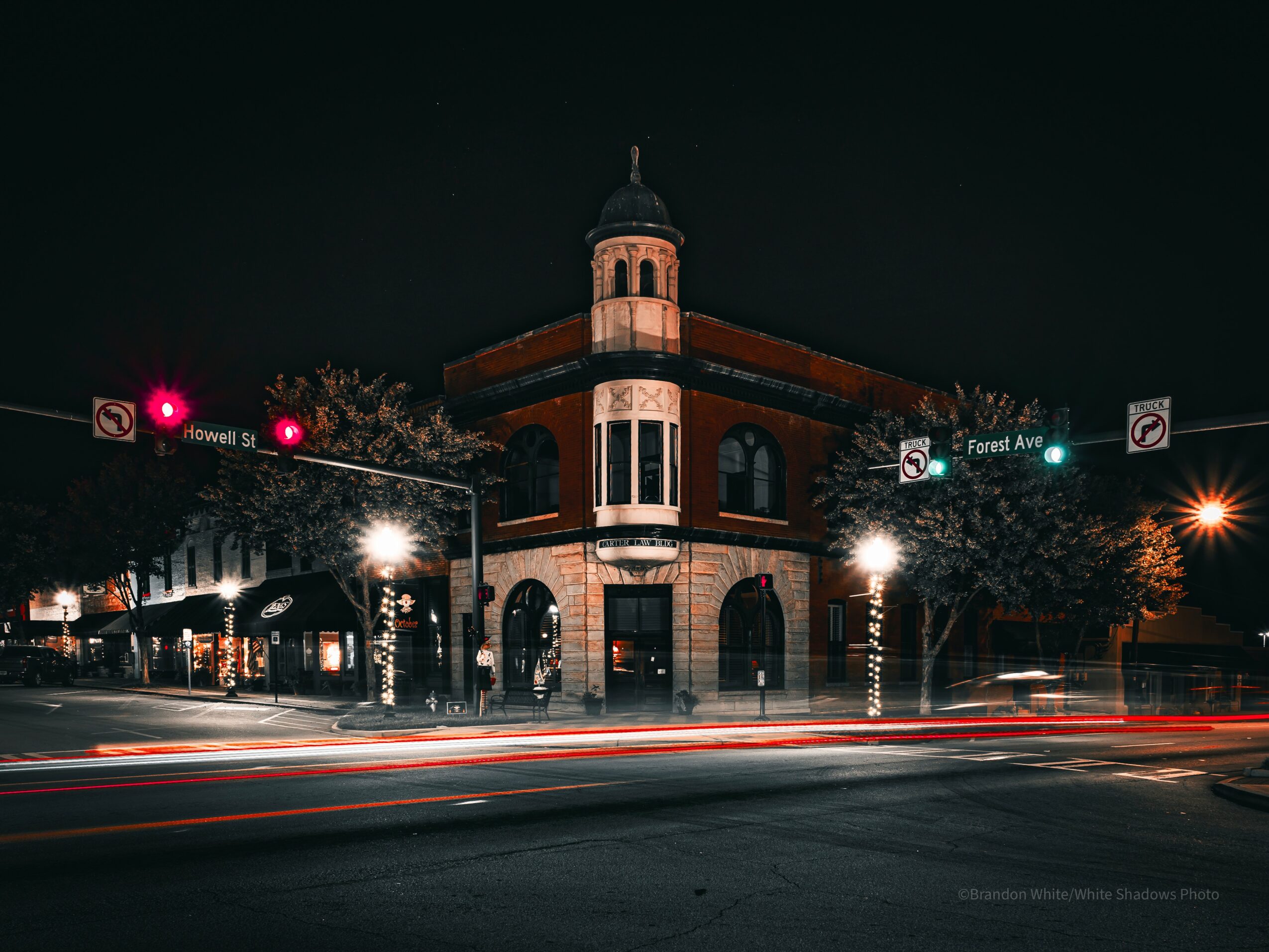 Nighttime city scene with a historic building, traffic lights, and light trails from passing cars.