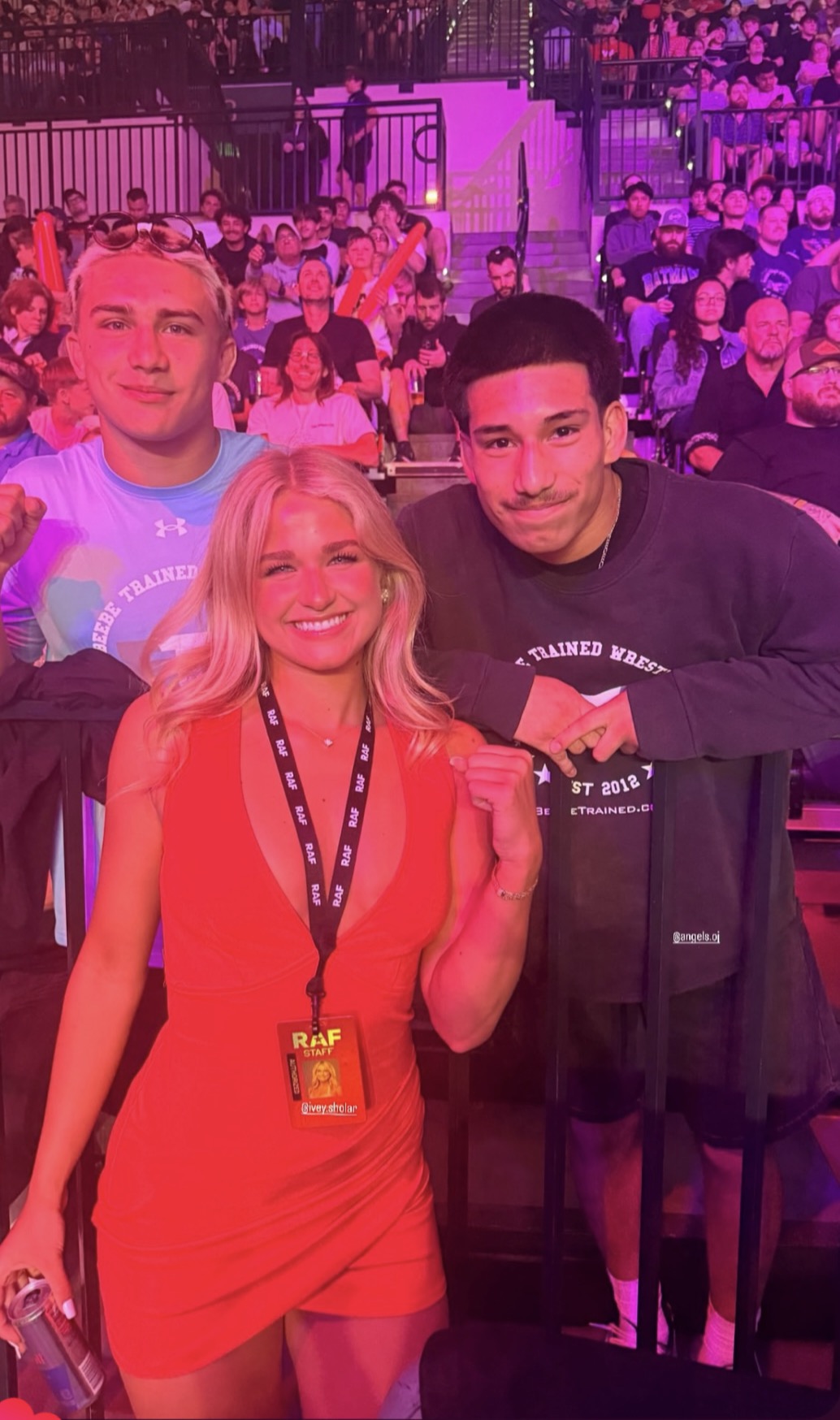 Three people smiling at an event, with a crowd and stage in the background.