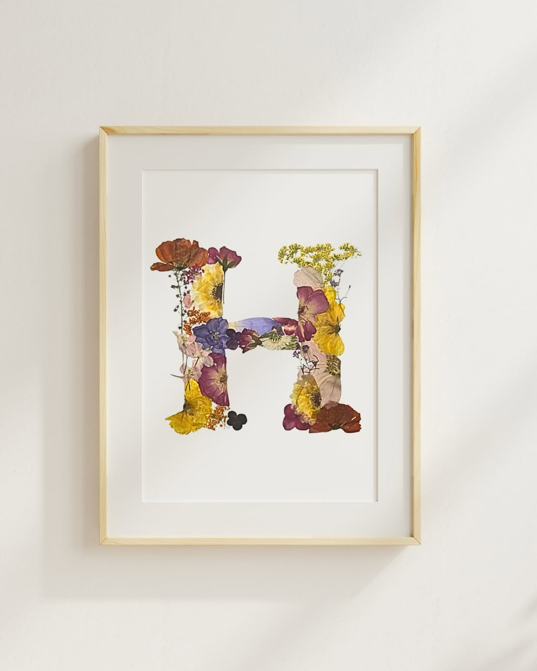 Framed watercolor painting of two abstract animals facing each other, with colorful patches and floral elements, on a white wall.