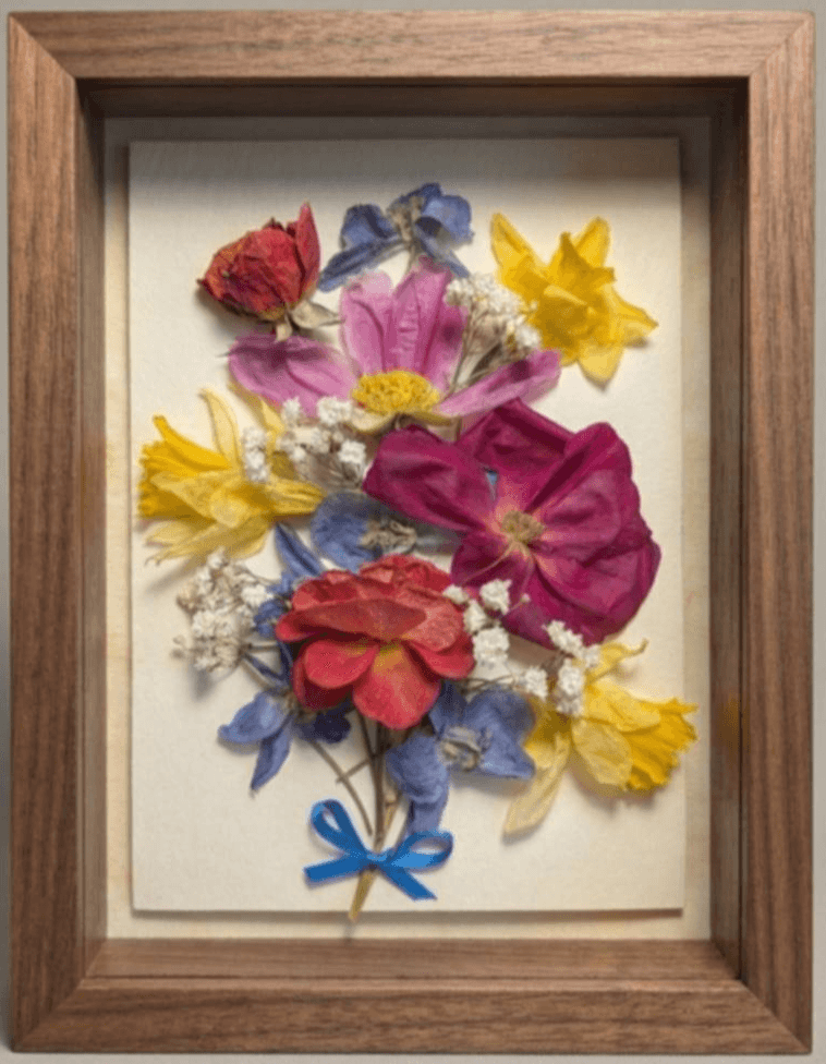 Pressed colorful flowers arranged with a blue ribbon in a wooden frame.