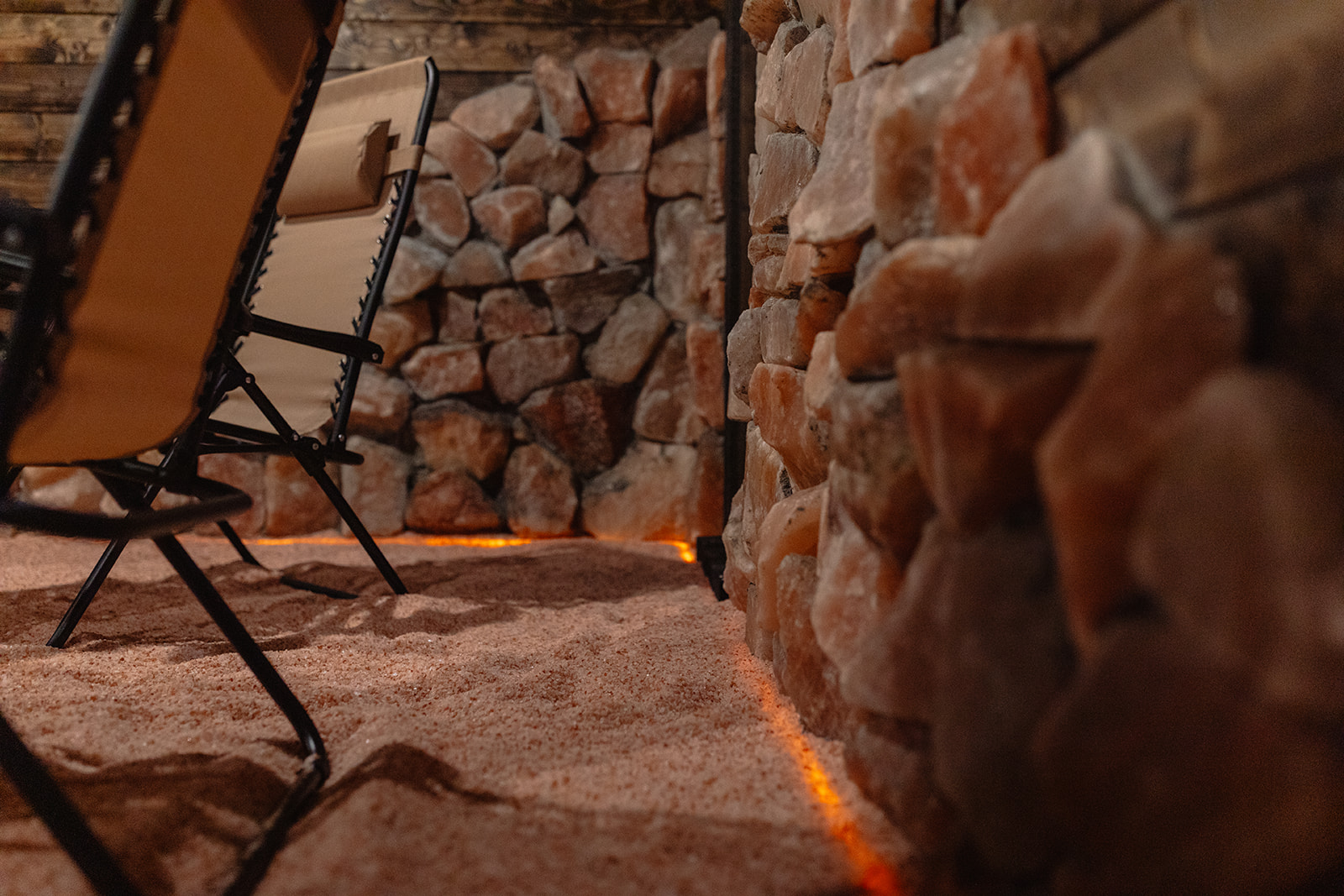 Close-up of a stone wall with warm lighting and a carpeted floor, with chairs in the background.
