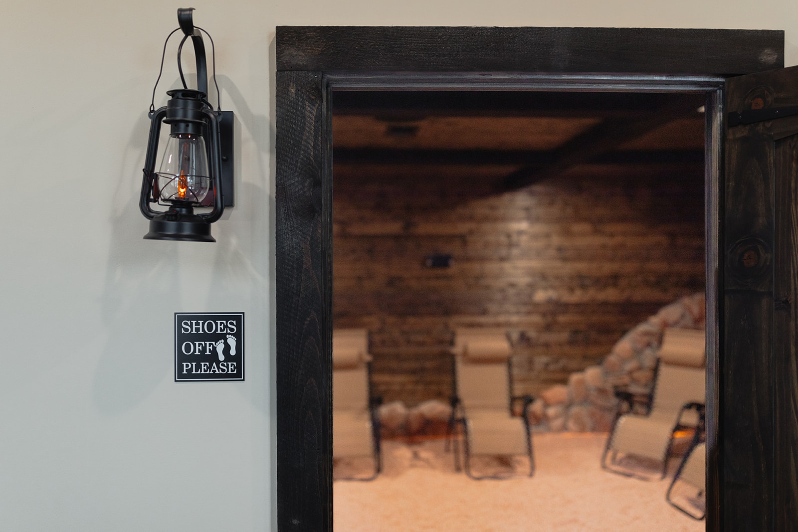 Open doorway leading to a room with wooden walls and chairs, lantern hanging on the wall, sign reading 'Shoes Off Please'.