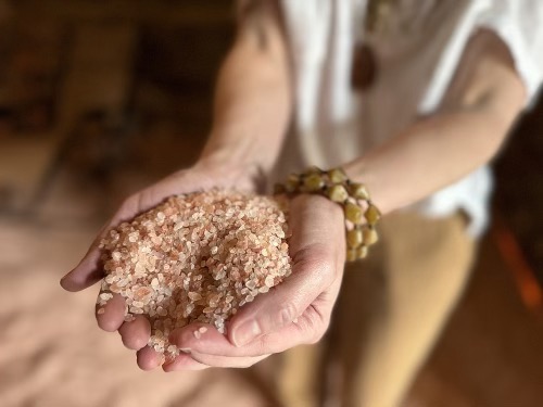Person holding a large, pinkish salt crystal in their hand, wearing a bracelet, with a blurred background.