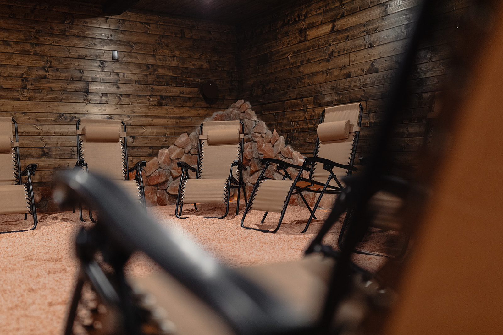 Indoor room with wooden walls, three beige chairs, and a rock formation, viewed from an angle.