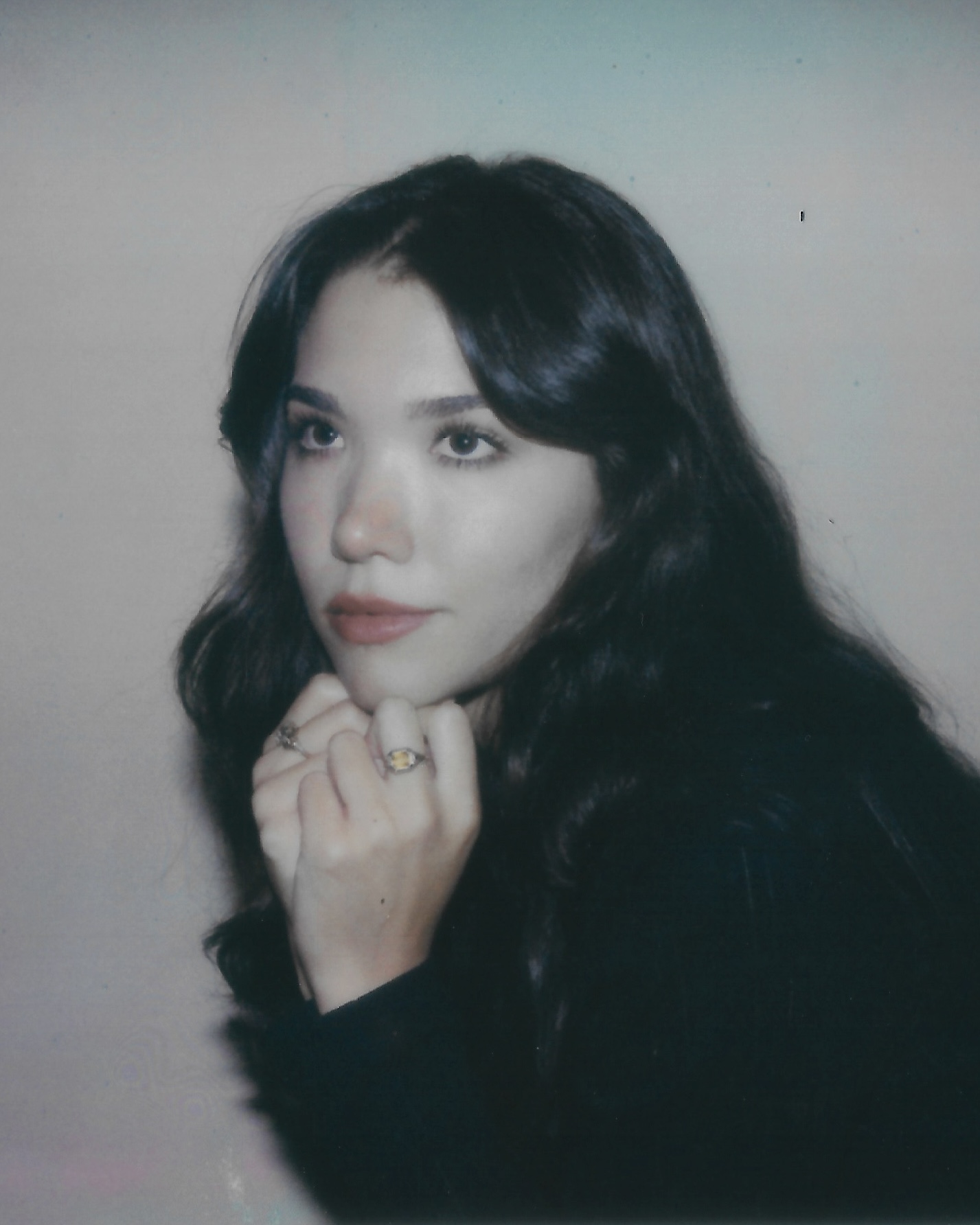Portrait of a woman with long dark hair, resting her chin on her hand, looking to the side.