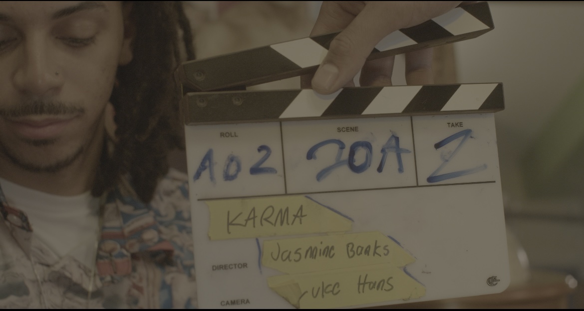 Person holding a clapperboard with handwritten text, partially visible face, and a blurred background.