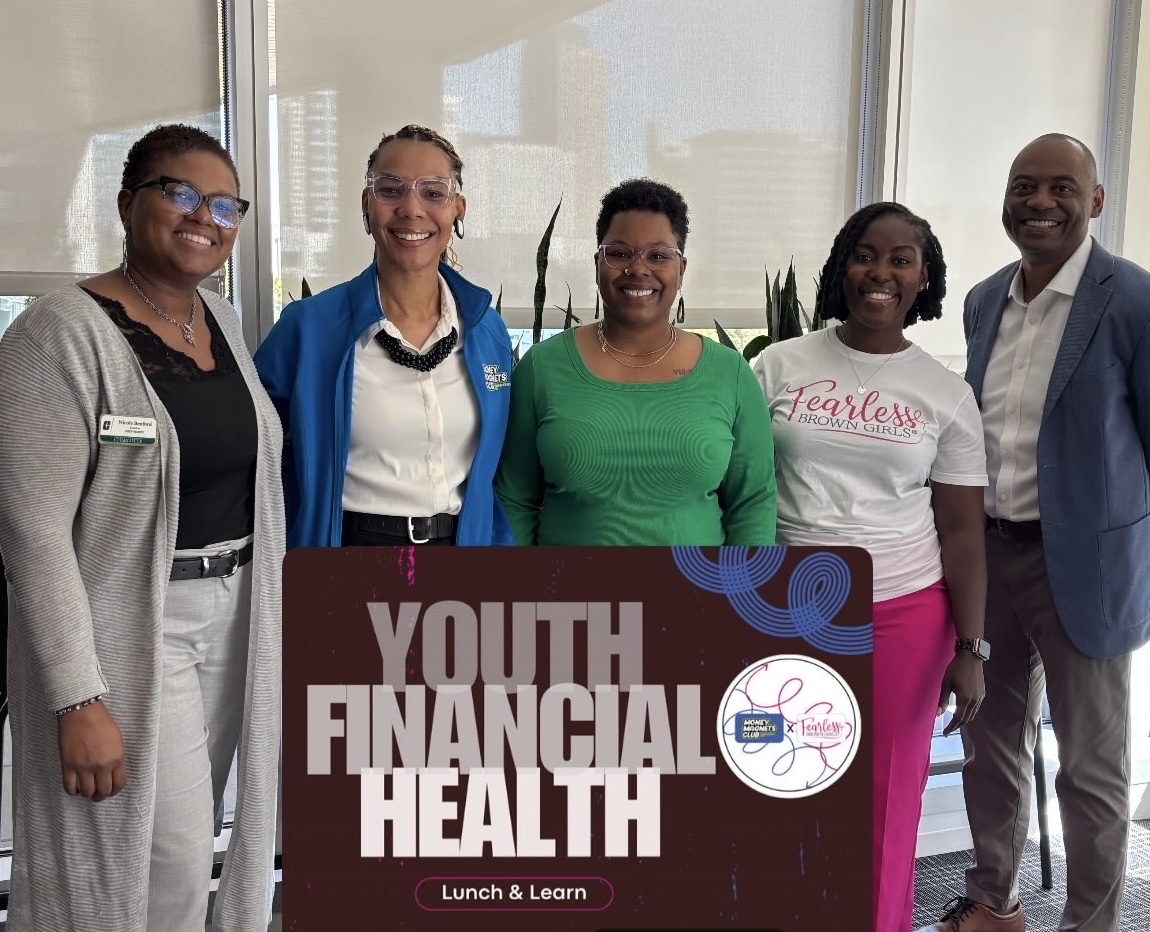 Group of six diverse people standing behind a sign that reads 'Youth Financial Health' at an indoor event.