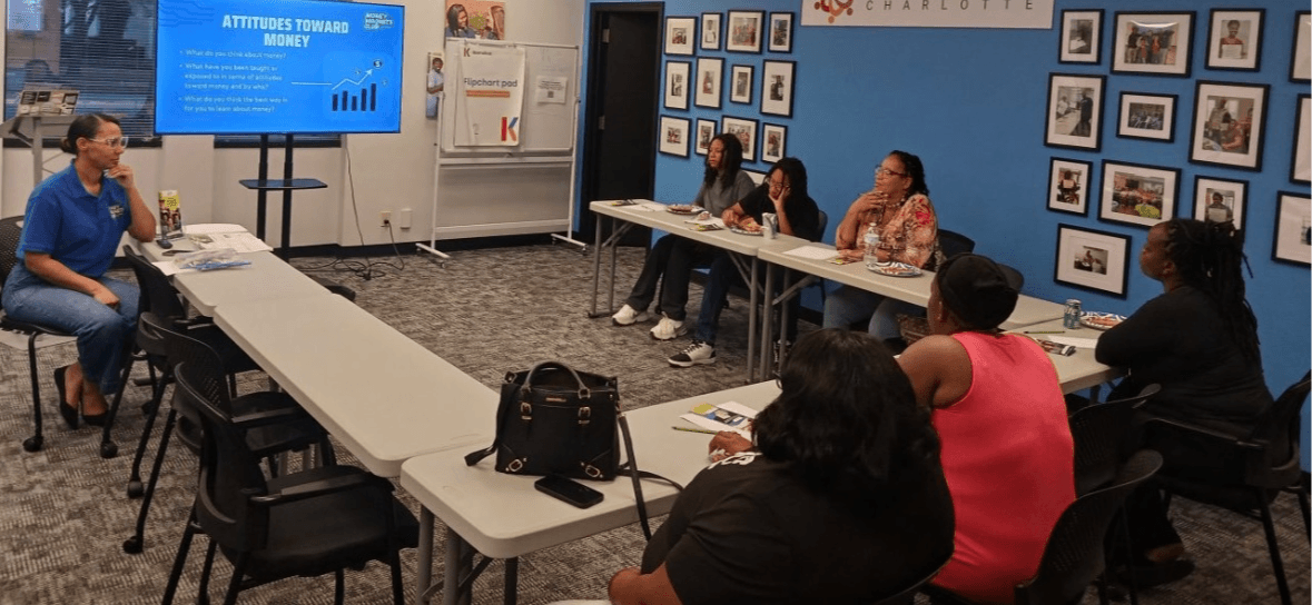 Person presenting to a group in a classroom with a large screen and framed pictures on the wall.