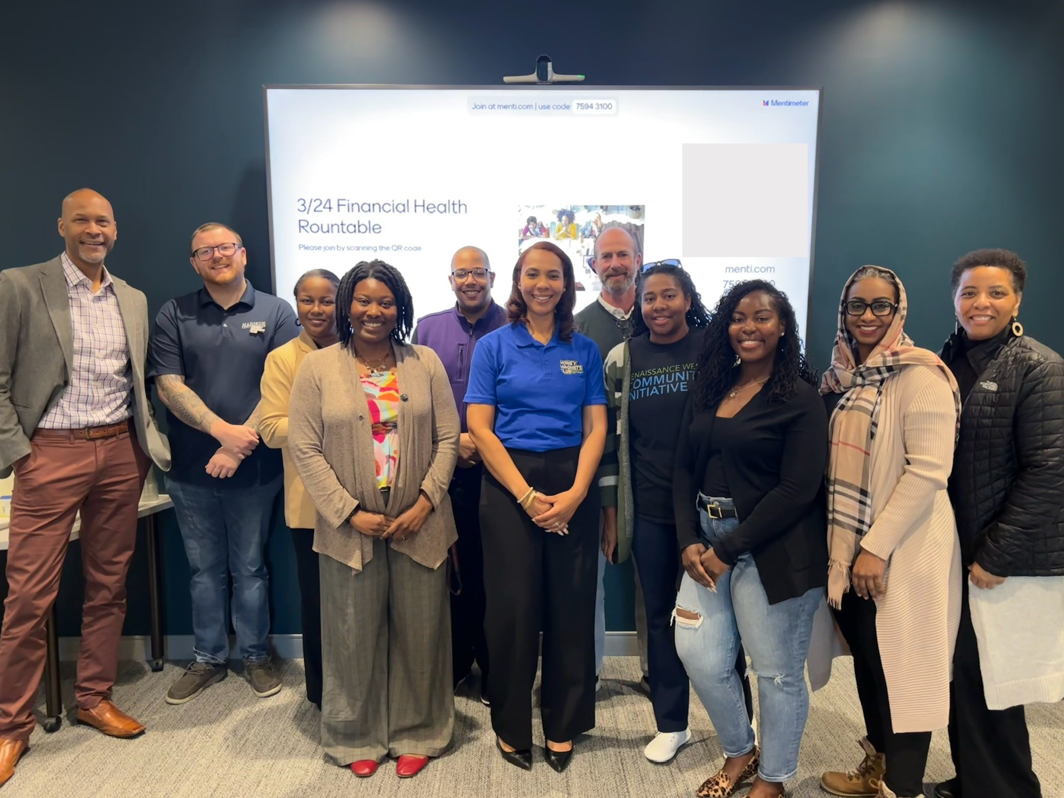 Group of ten people standing in front of a presentation screen at a professional event, smiling and posing for the photo.