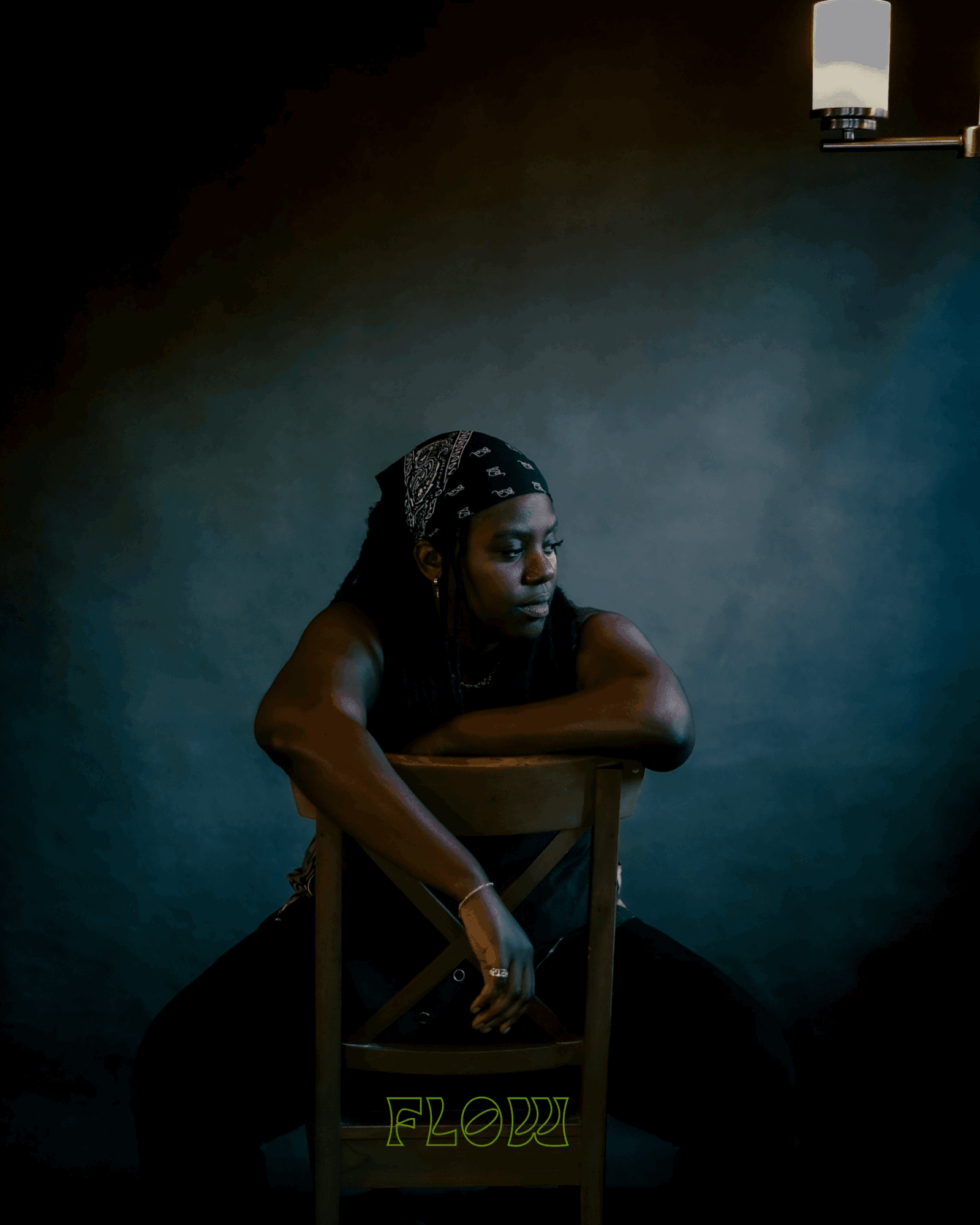 Person with a bandana resting on a chair, dark background, small light source above, contemplative expression.