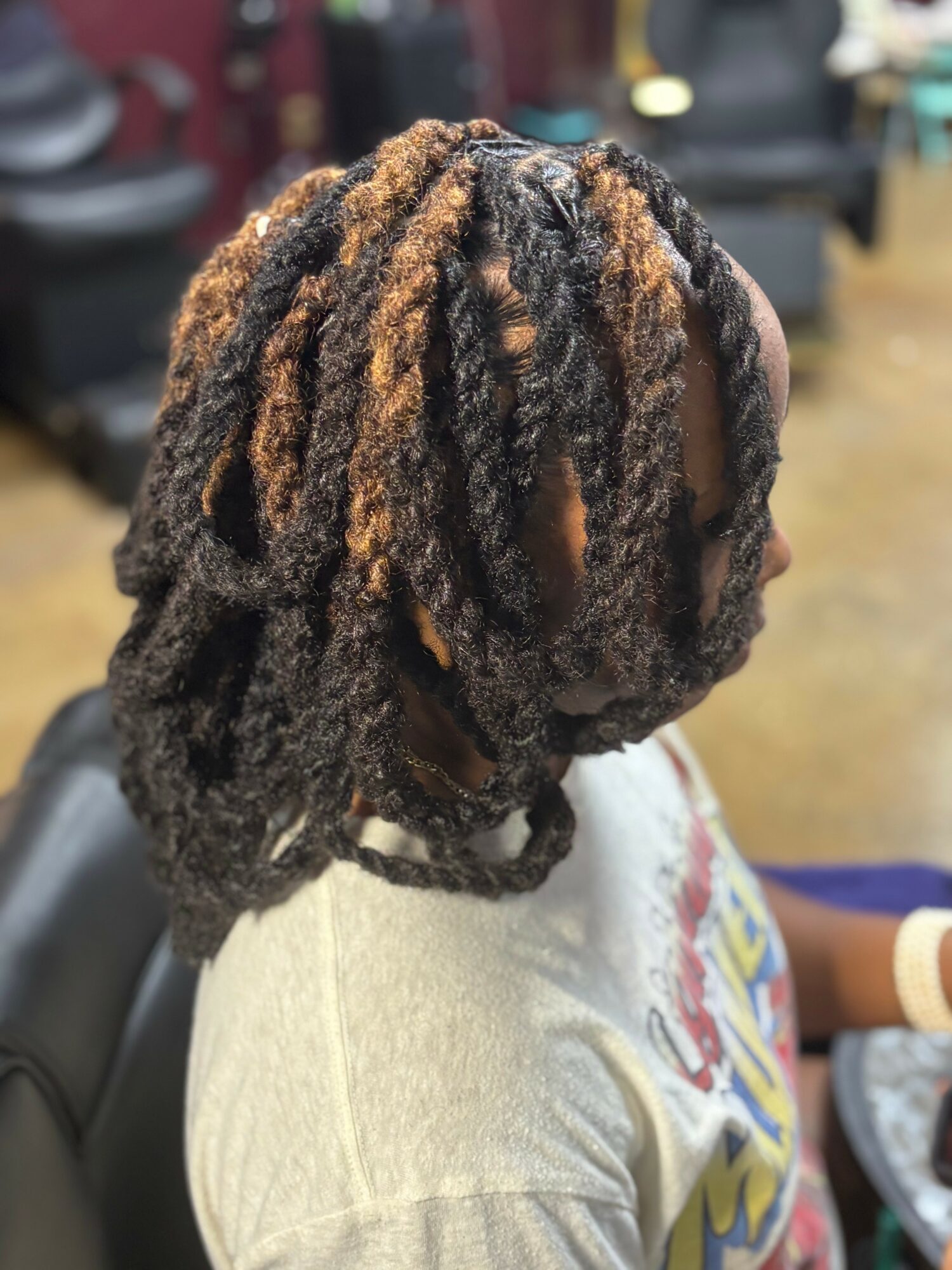 Side view of a person with styled dreadlocks, wearing a light-colored shirt, in an indoor setting.