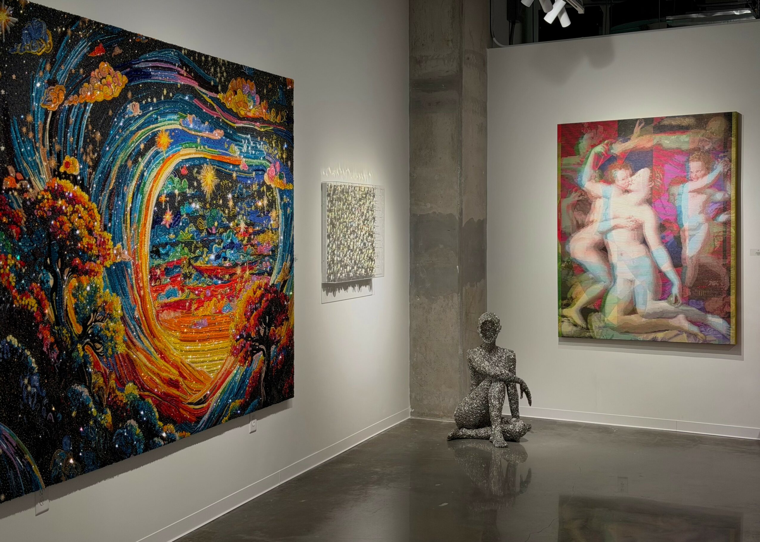 Gallery with colorful paintings on white walls, a sculpture of a seated figure, and a concrete pillar.